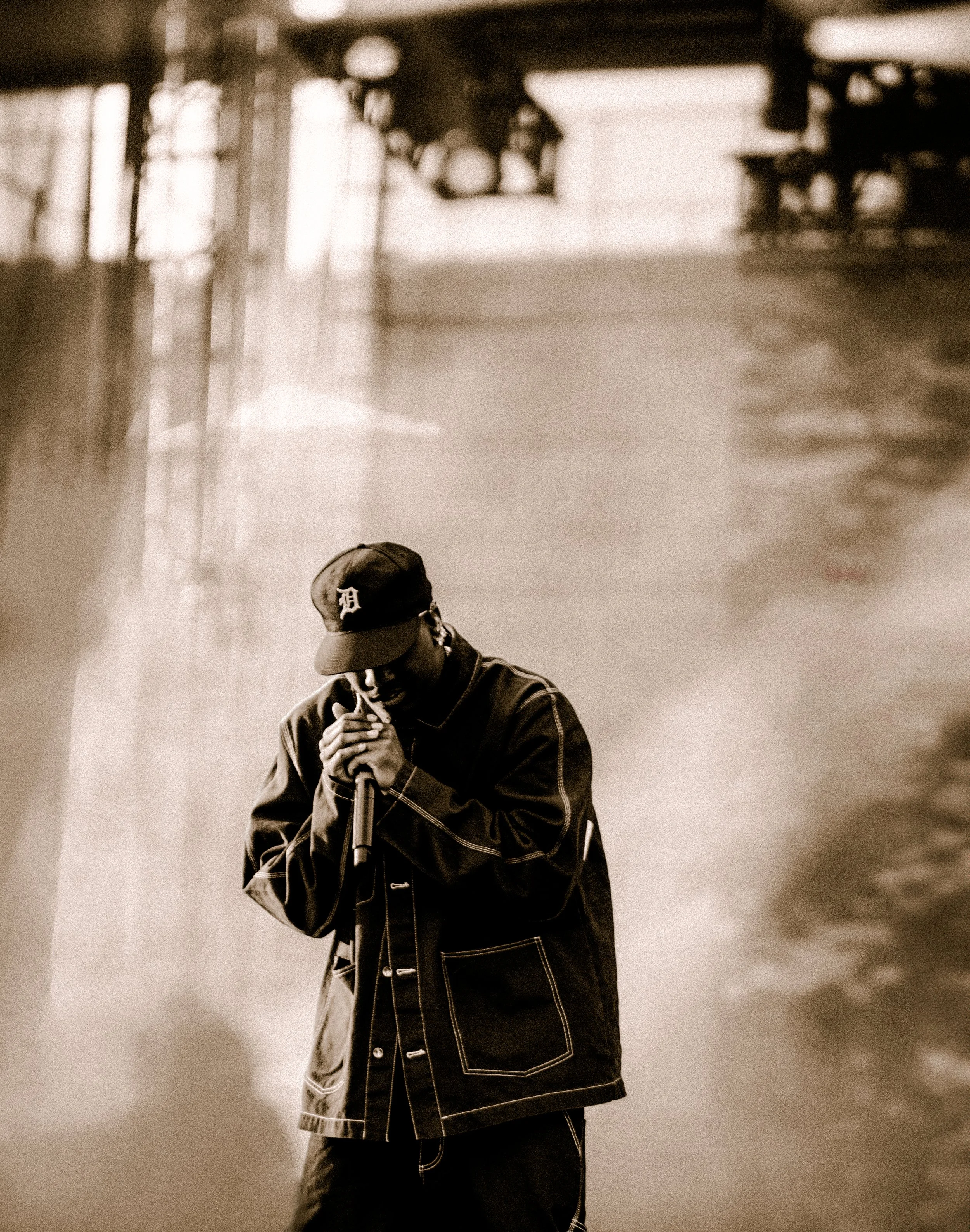 Musician performing on stage with a microphone, wearing a black jacket and cap.