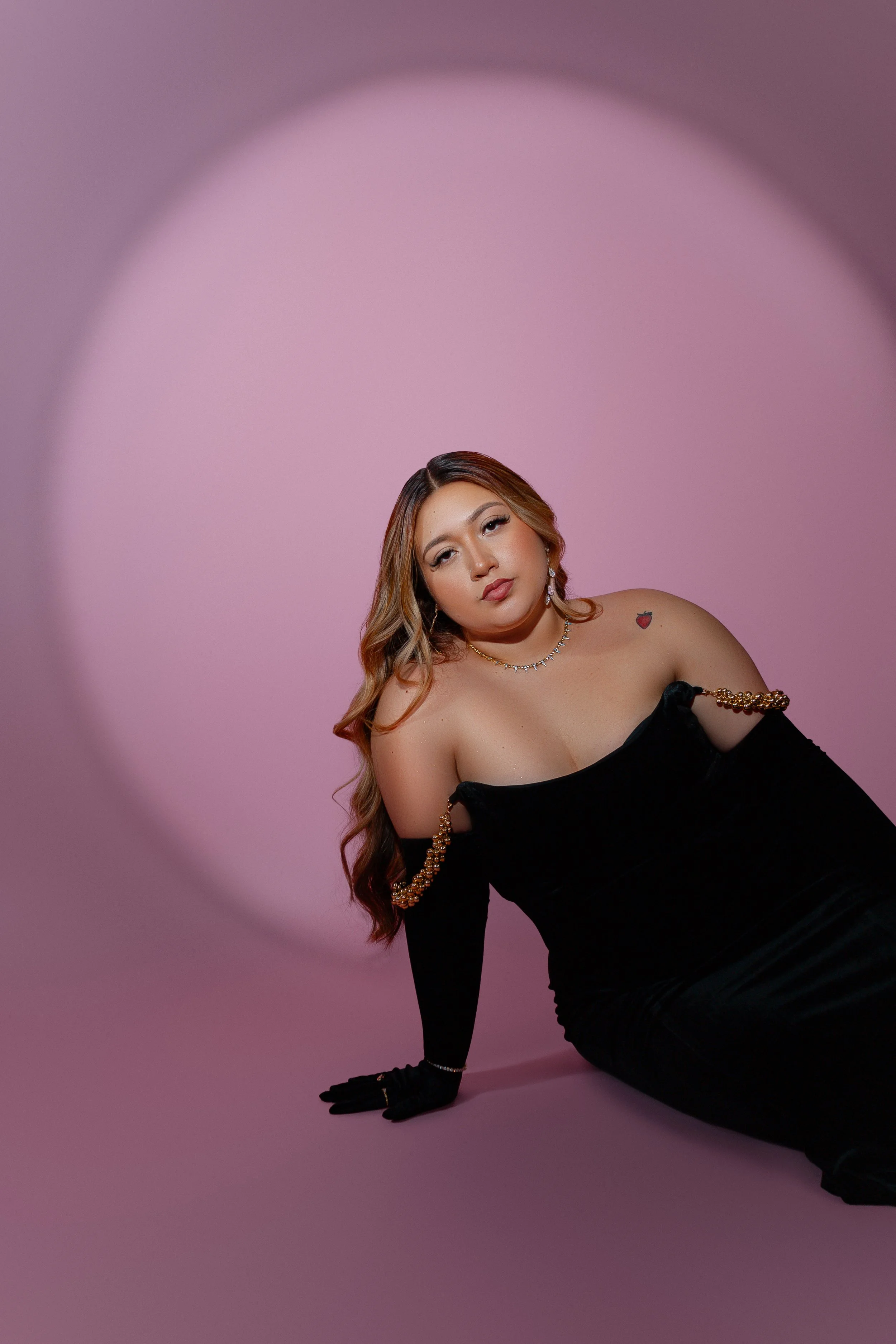 Person in a black dress posed against a pink background.