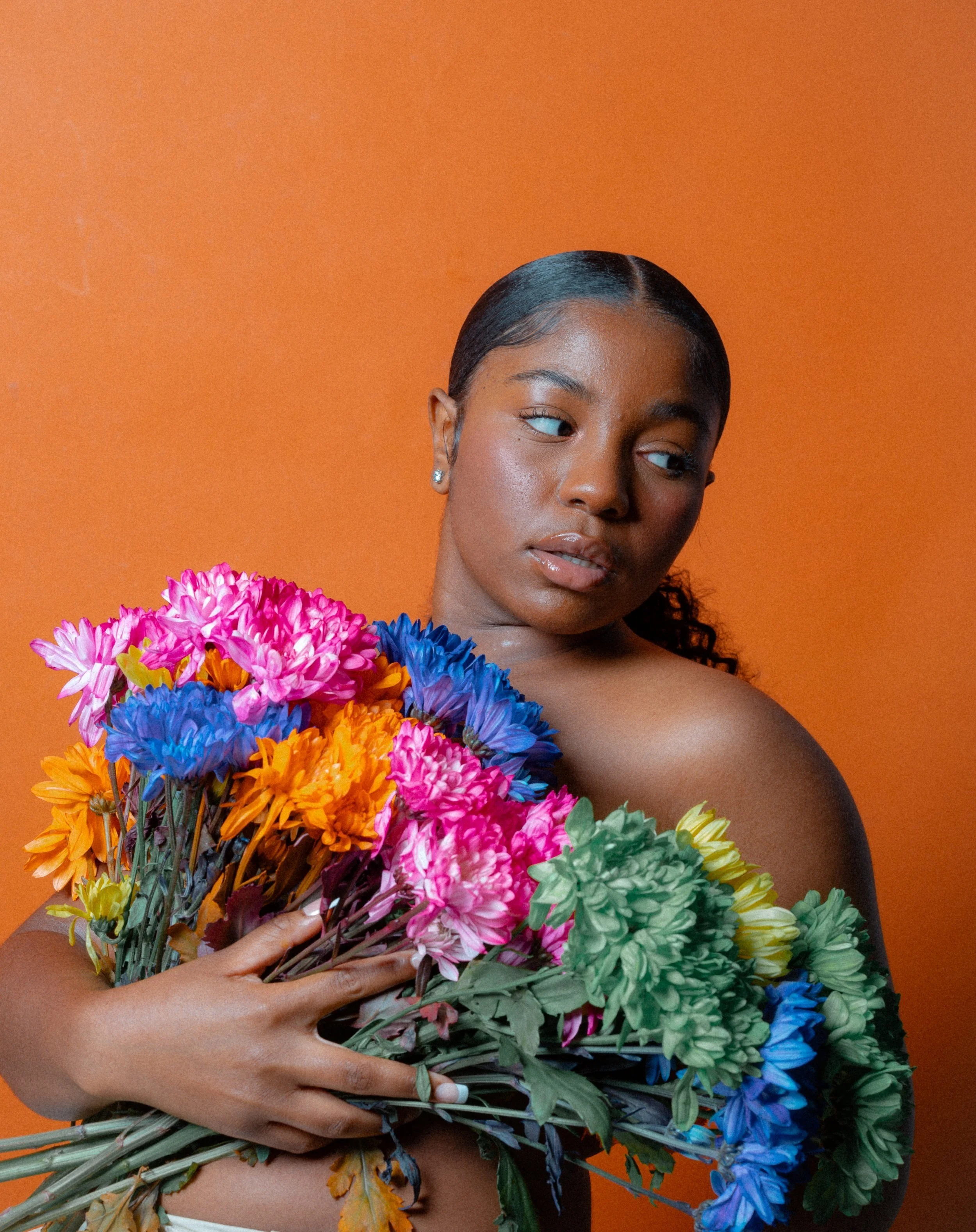 A person holding a bouquet of colorful flowers against an orange background.