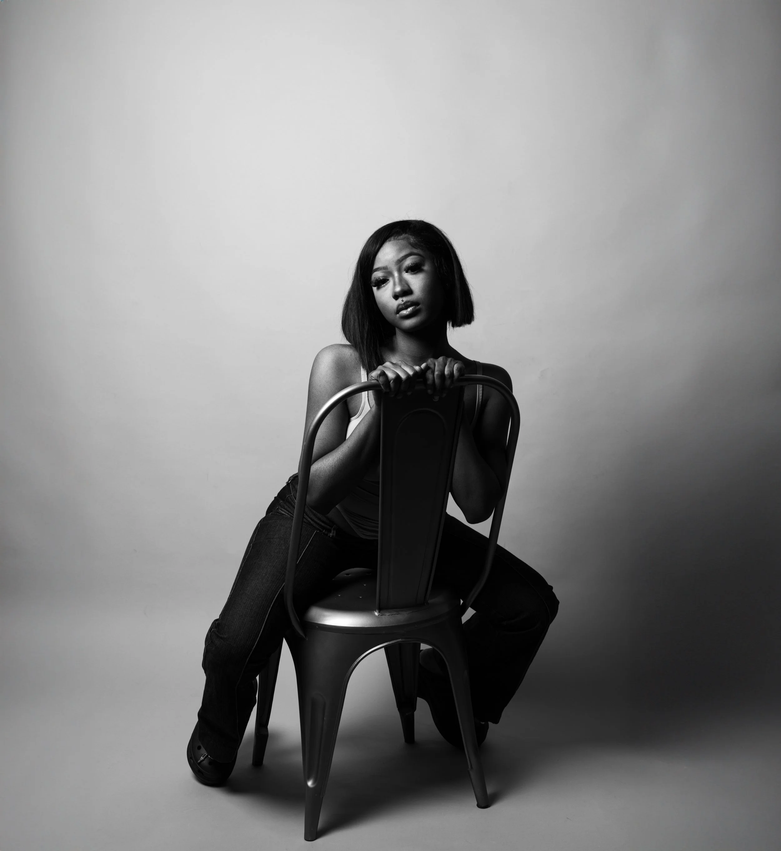 Black and white photo of a woman sitting backward on a chair, looking contemplative.