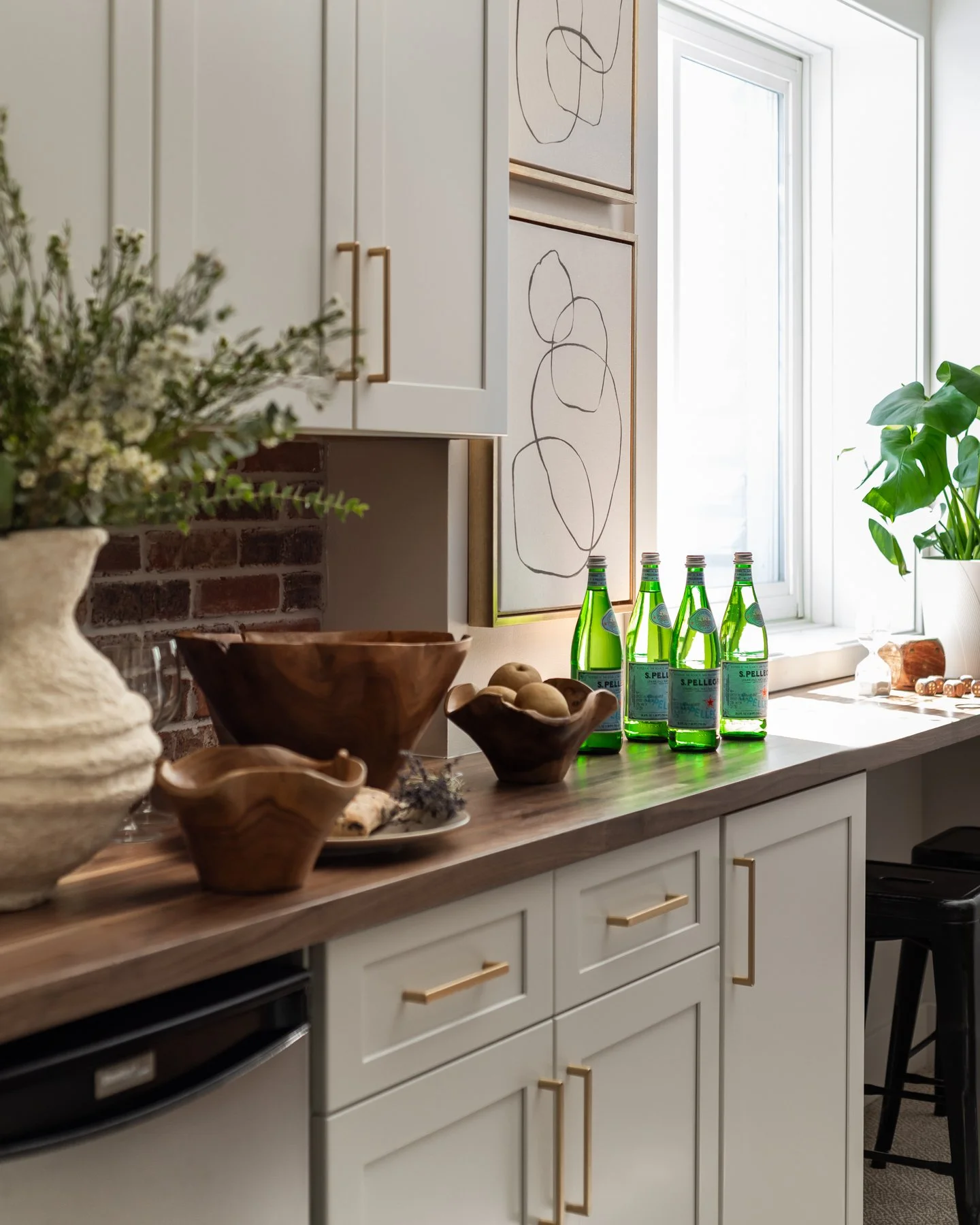 Kitchen countertop with decorative bowls, a vase of flowers, and green bottles of soda near a window with sunlight.