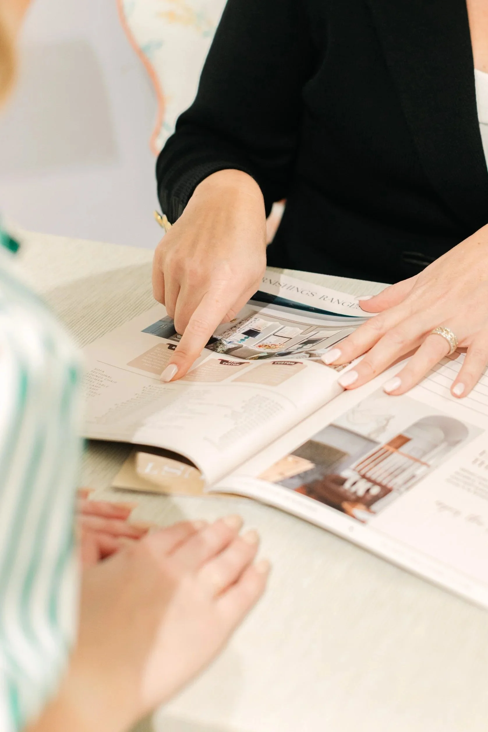 People looking at and pointing to a magazine or brochure on a table.