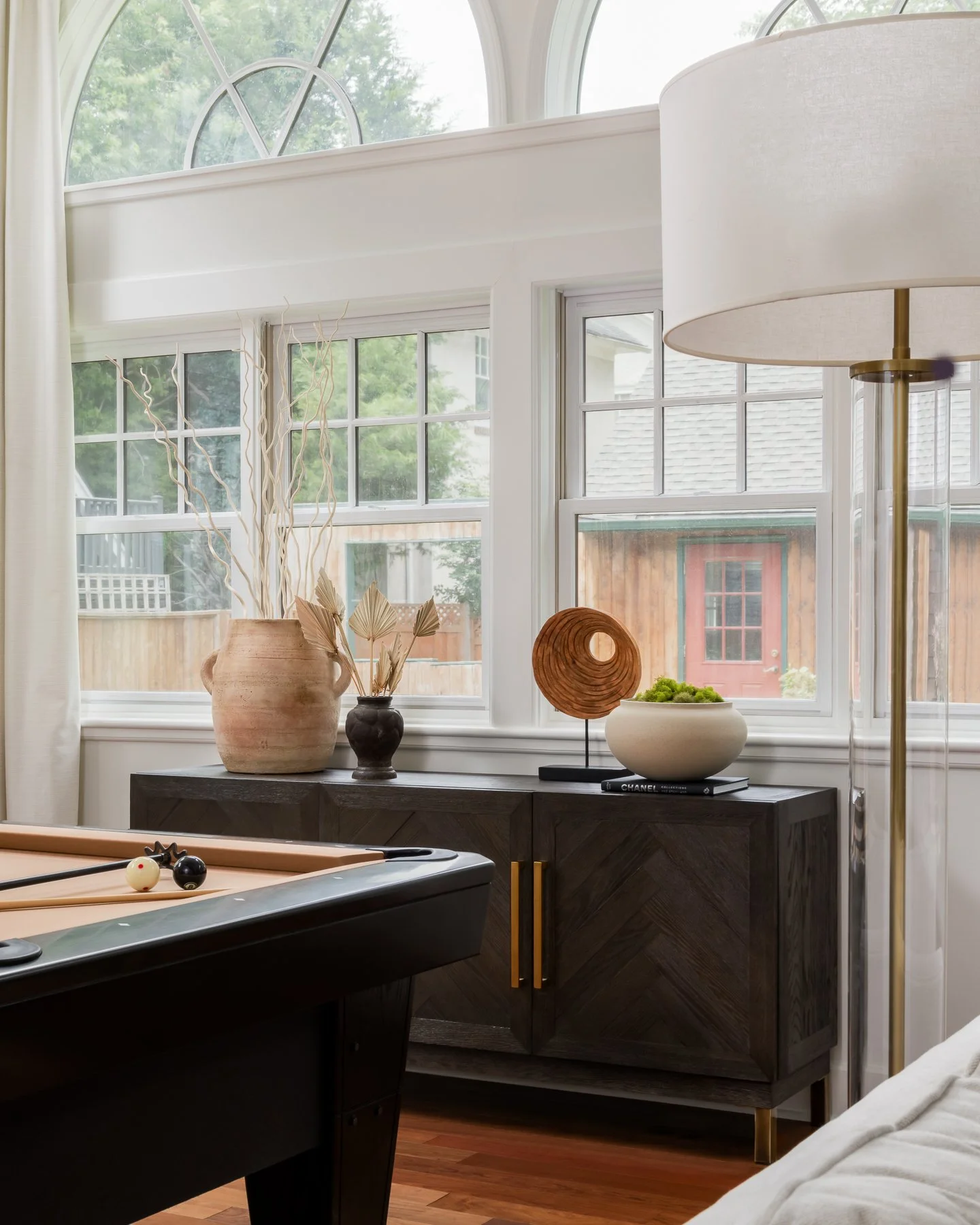 Interior of a room with large windows, decorative vases on a black cabinet, and a pool table in the foreground.