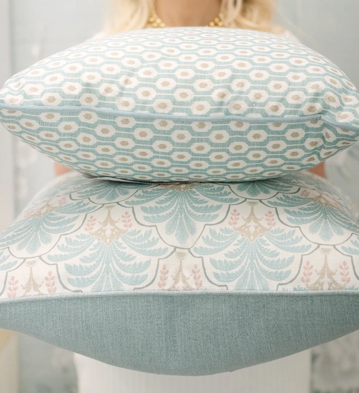 Close-up of three decorative pillows with pastel patterns: the top pillow has a geometric pattern, the middle pillow has a floral design, and the bottom pillow has a solid color with a textured fabric.