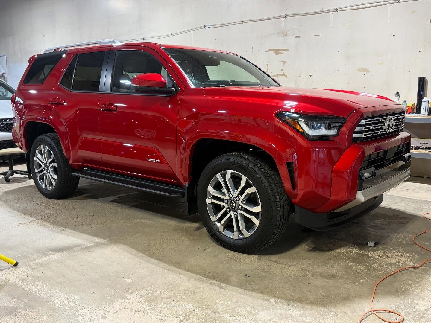 Red Toyota SUV parked indoors with a concrete floor and wall in the background. The SUV has black accents and silver rims.