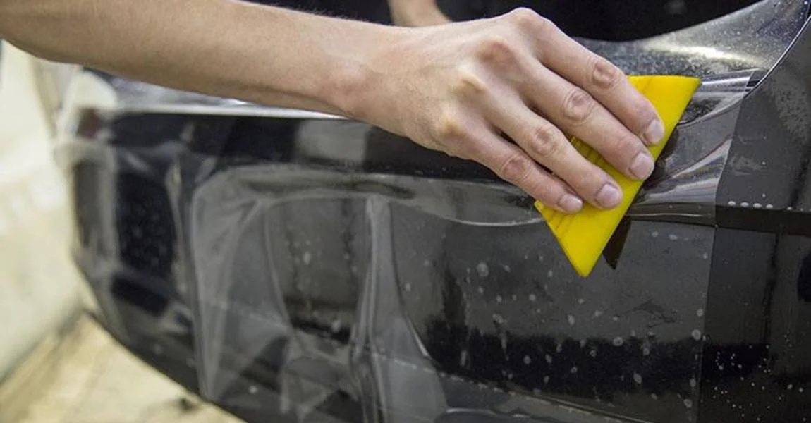 Person using a yellow squeegee to apply paint protection film