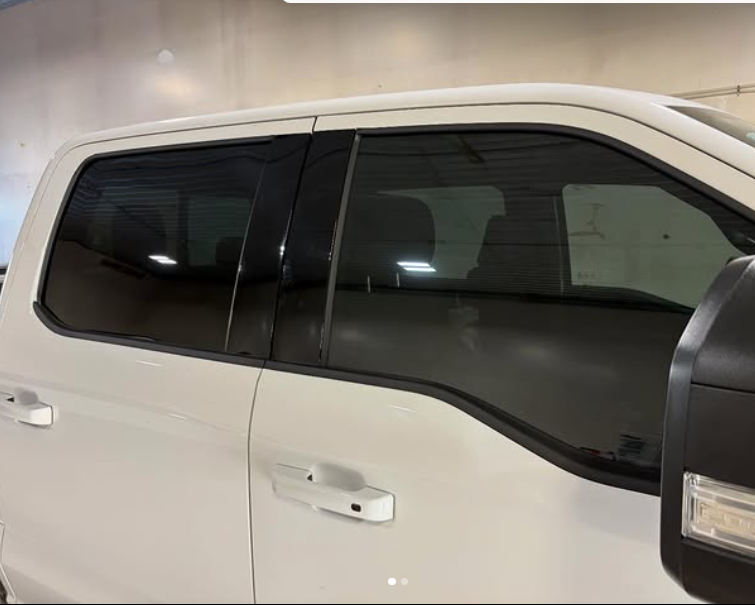 Close-up of the side of a white pickup truck, showing tinted windows and door handles.