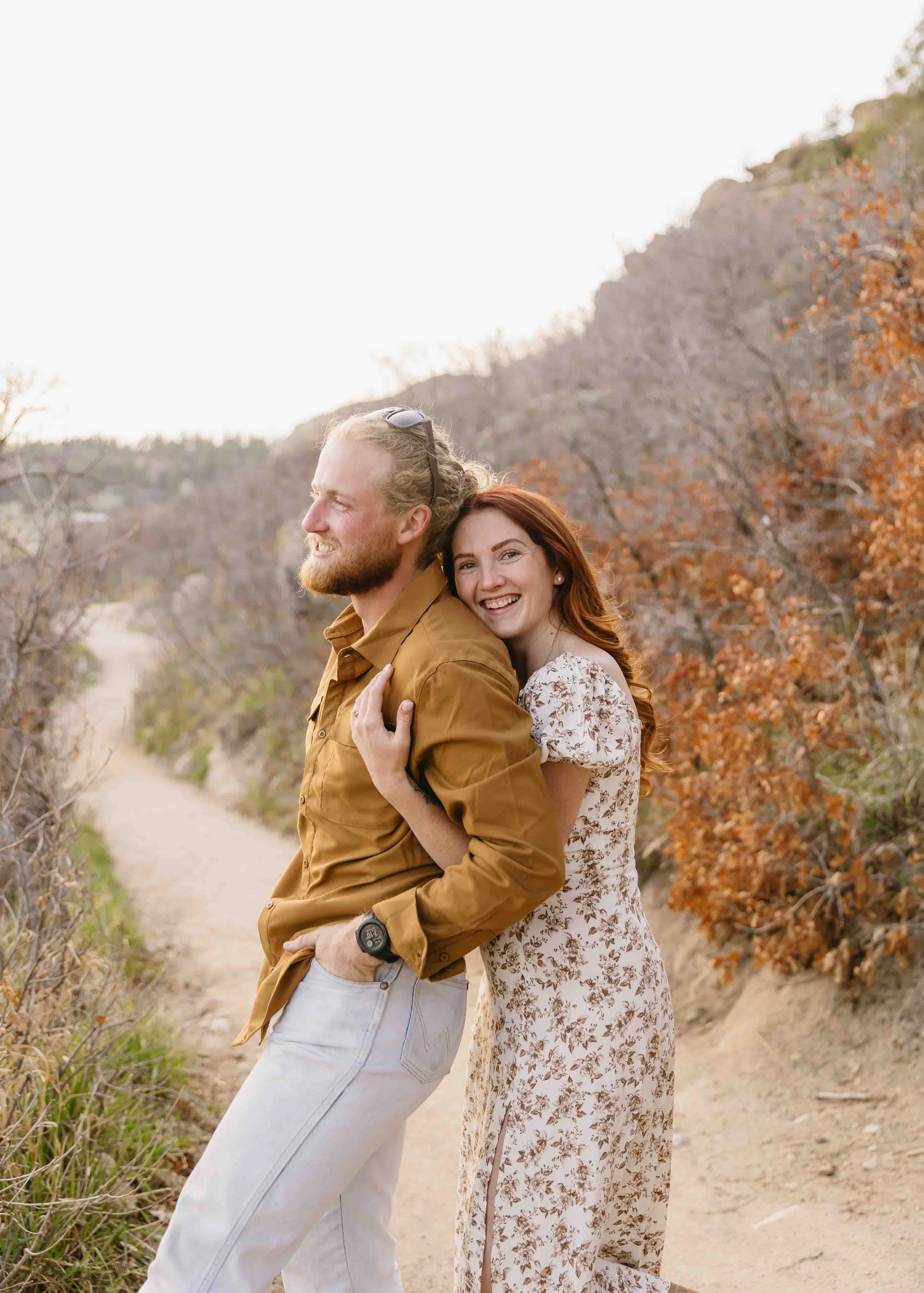 A man and woman embrace during their engagement shoot in the colorado mountains, golden light turns into blue hour for tender, loving and fun engagement session