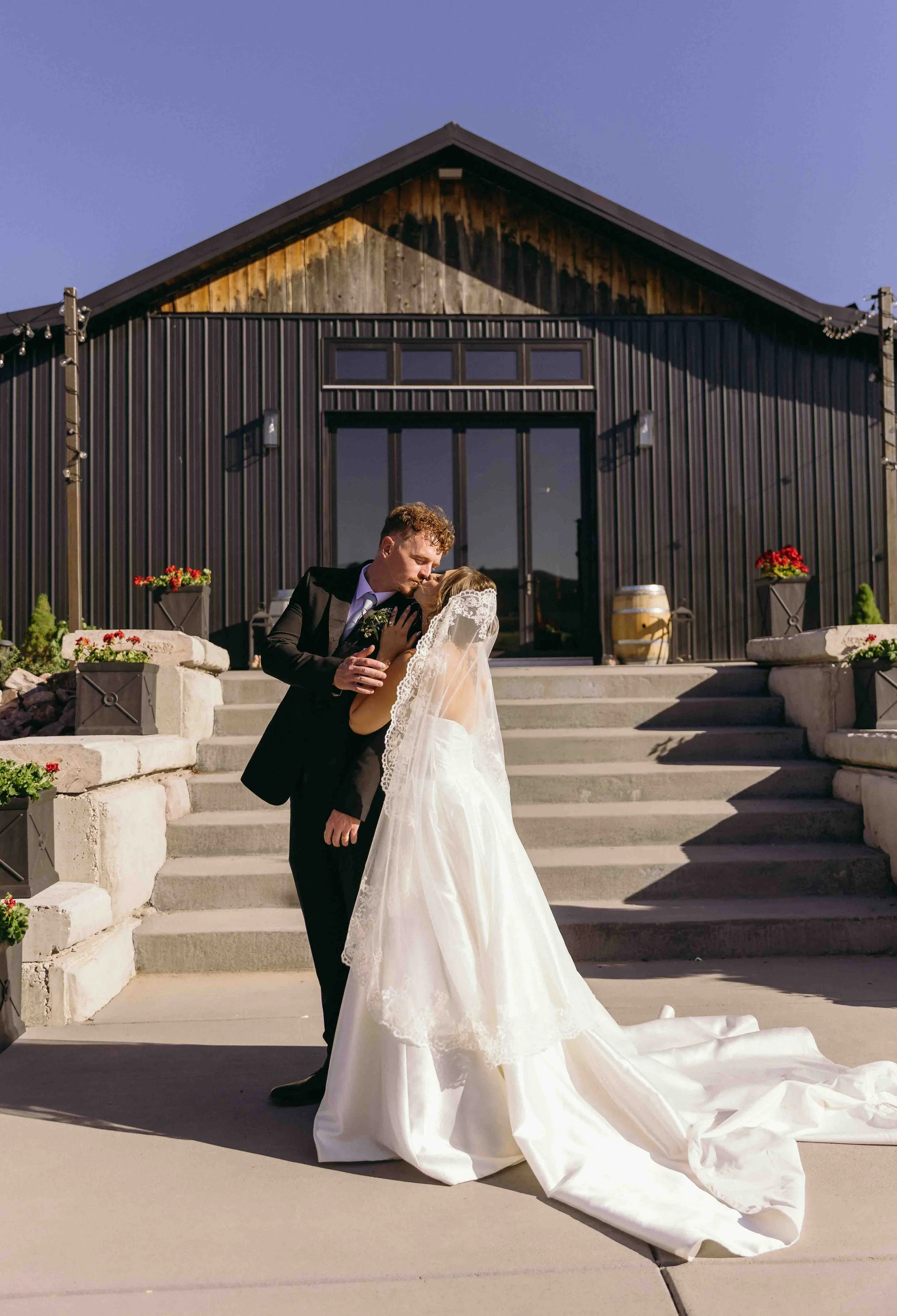 a vintage inspired couple who love books and ducks kiss in front of their venue Marchand Ranch shortly after their summer wedding ceremony