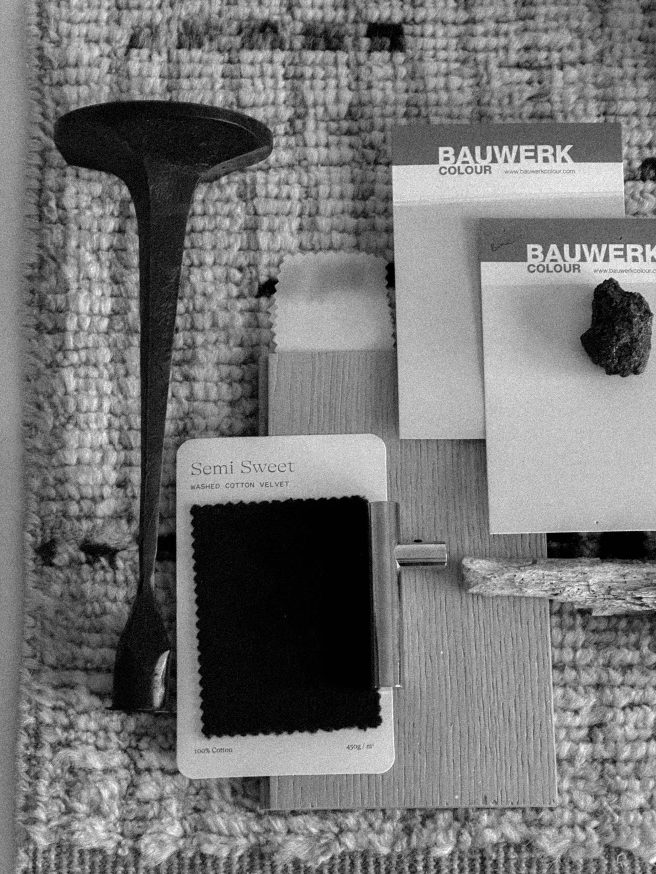 Different fabric swatches and color samples on a textured surface, with a small block of wood, a metallic roller, and a textured stone in the background.