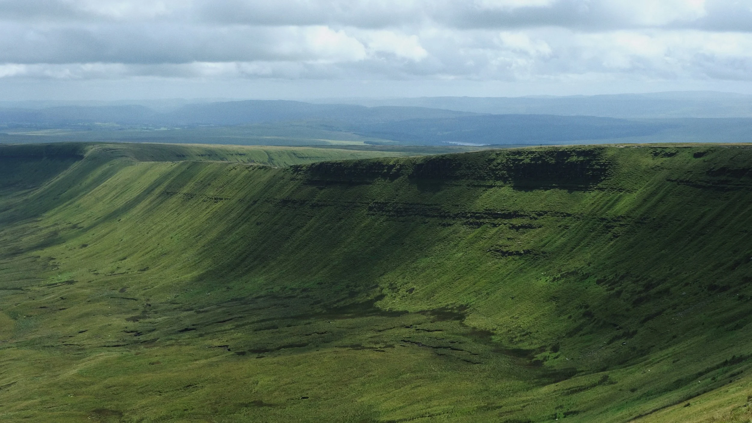 Green valley with steep cliffs and rolling hills under a cloudy sky.
