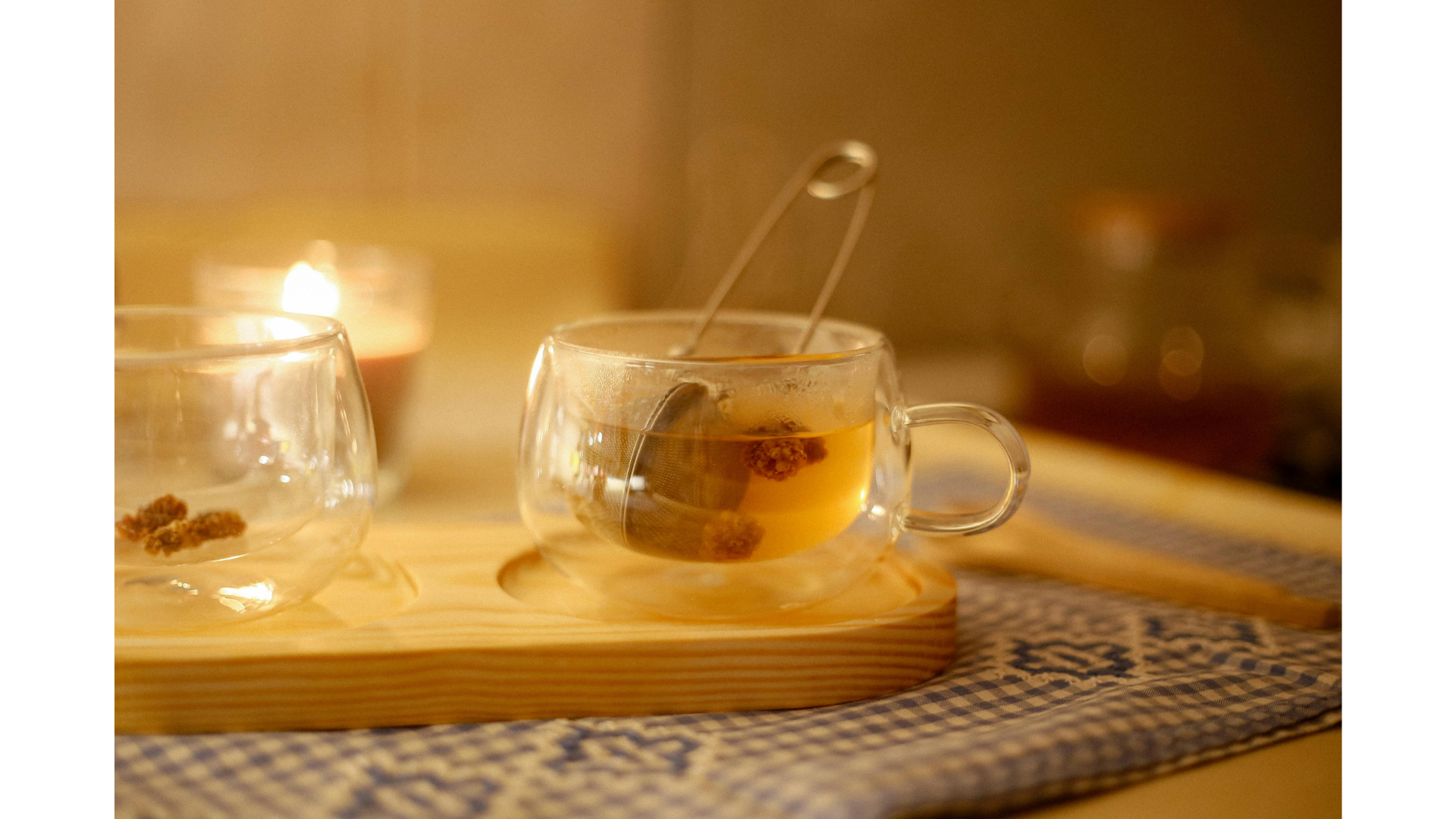 A relaxing moment of loose leaf tea steeping in a mesh ball in a glass mug with a candle in the background.