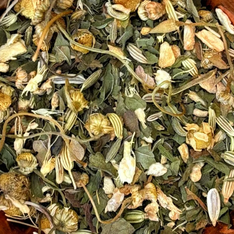 A close-up of dried herbal tea blend containing various dried flowers and leaves of chamomile, peppermint, ginger and fennel.
