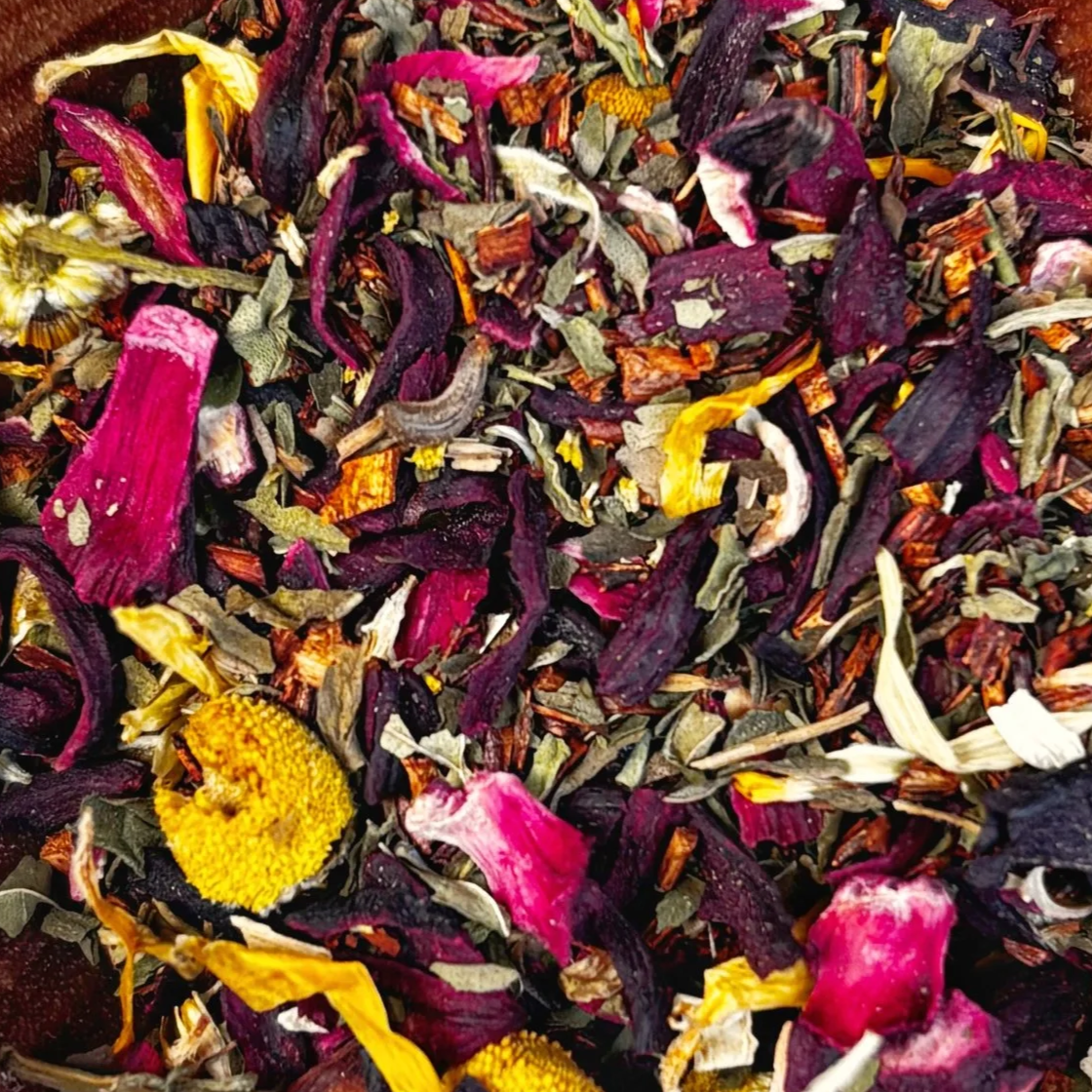 Close-up of dried loose herbal or floral tea with purple, yellow, pink, green, and white petals and flower parts of hibiscus, chamomile, calendula.