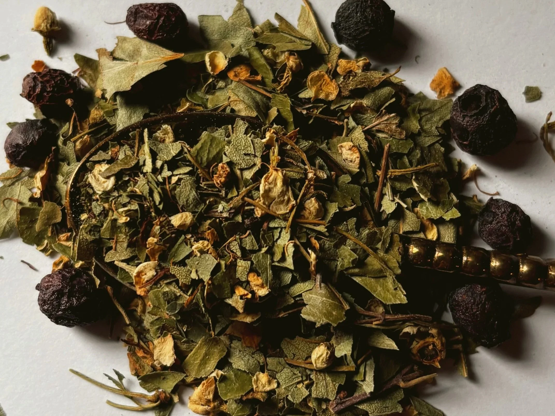 Dried loose hawthorn berry, leaf and flower on a gold spoon.