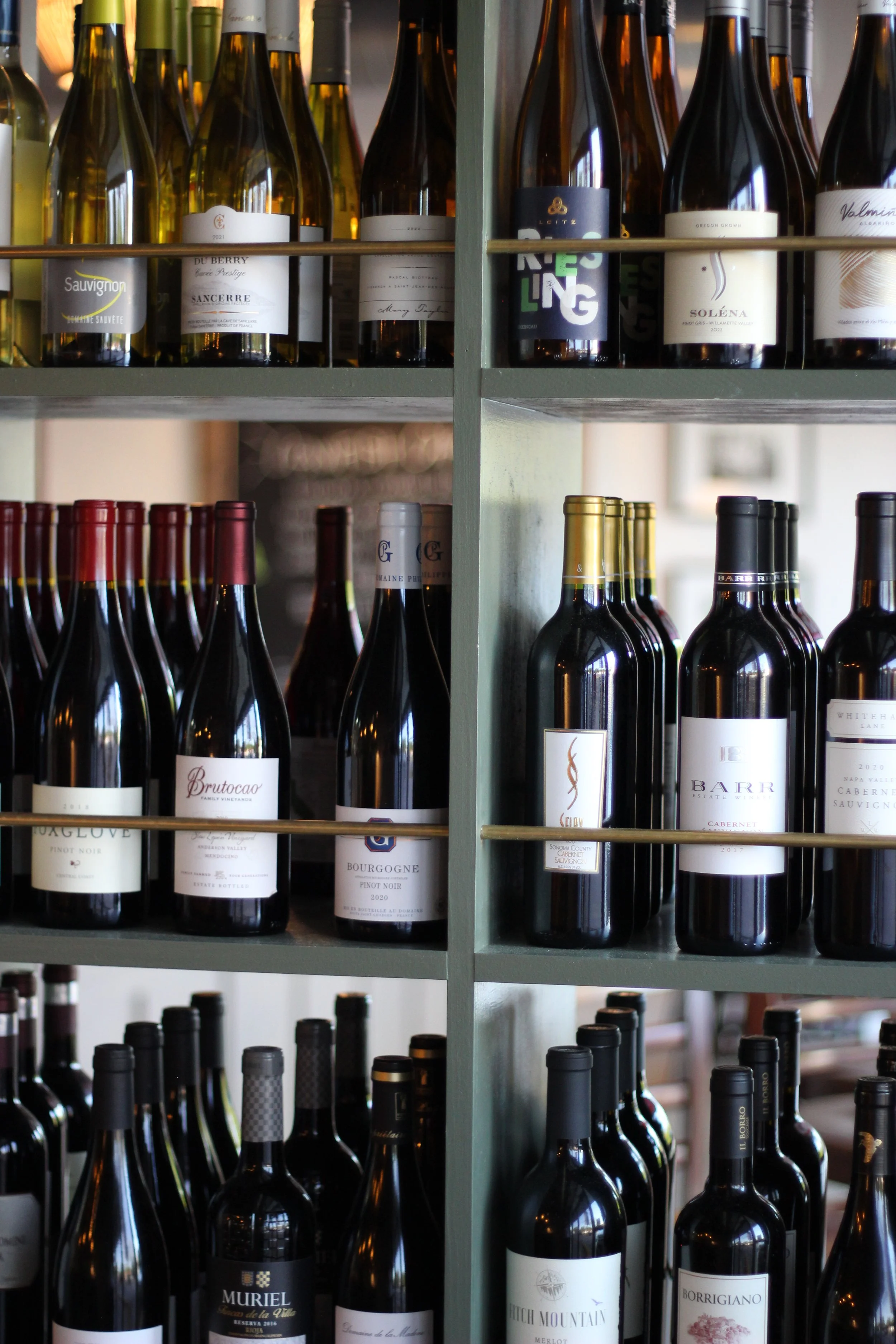 Red and white wines on sage green shelving at JED’s Local, available for private event bar packages
