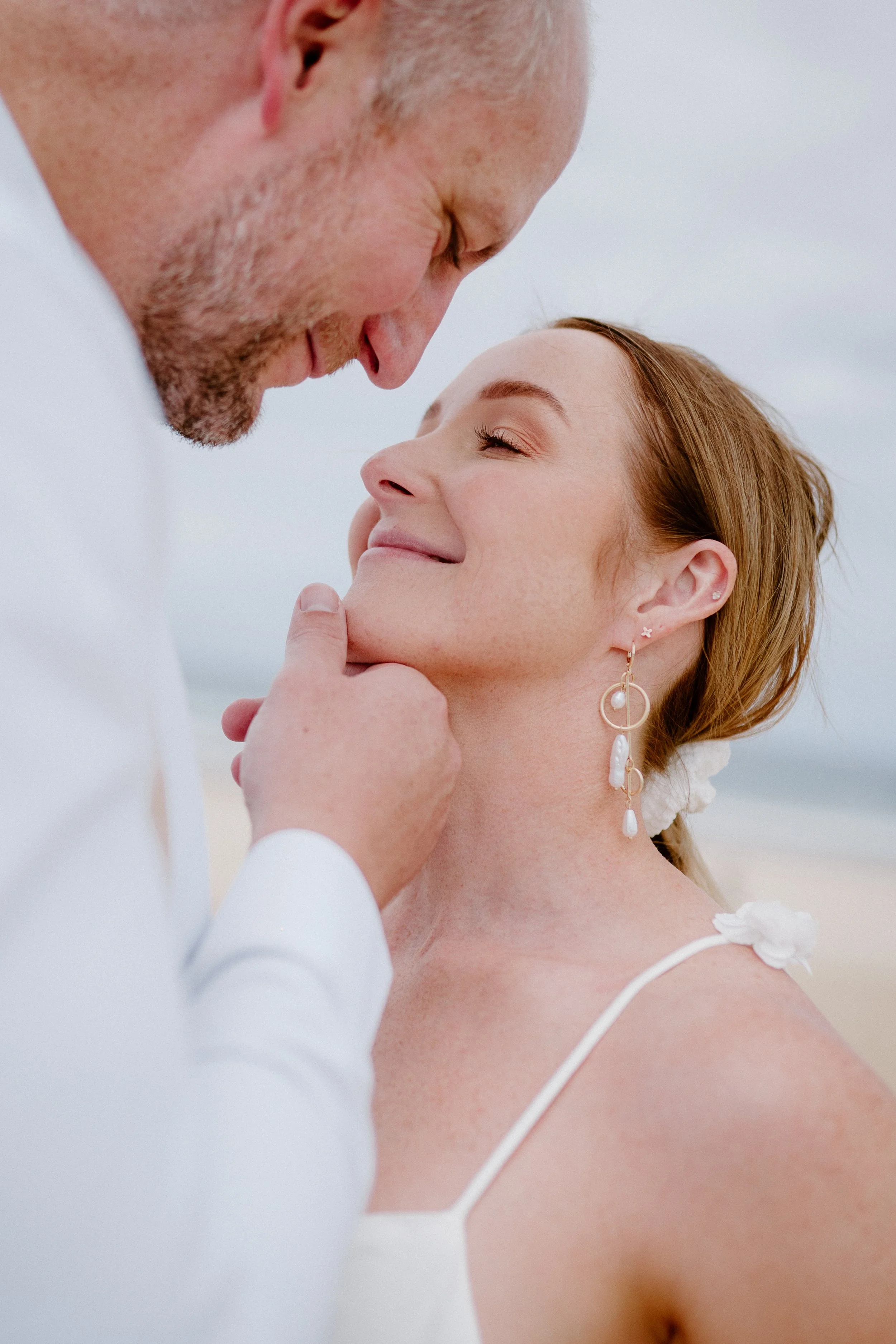 A man and woman sharing a close, intimate moment outdoors, with the man gently holding the woman's chin as they look into each other's eyes.