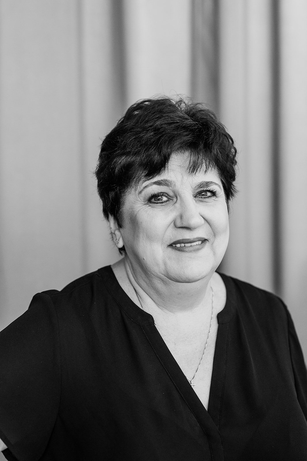 Black and white portrait of a woman with short hair, wearing a black top and a necklace, smiling at the camera.