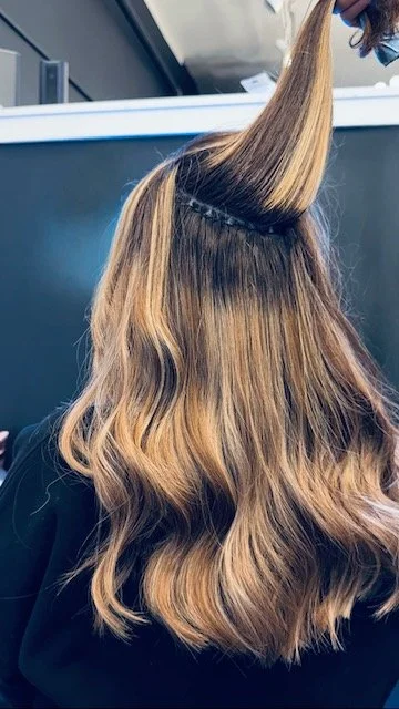 A woman getting her hair styled, with her hair partially curled and a section lifted for treatment or cutting.