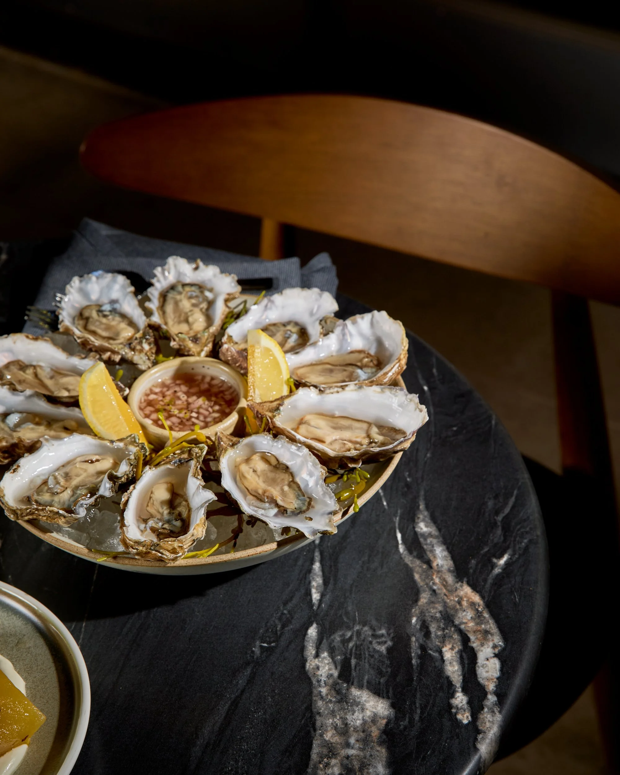 A plate of raw oysters on ice with lemon wedges and seafood sauce in the center.