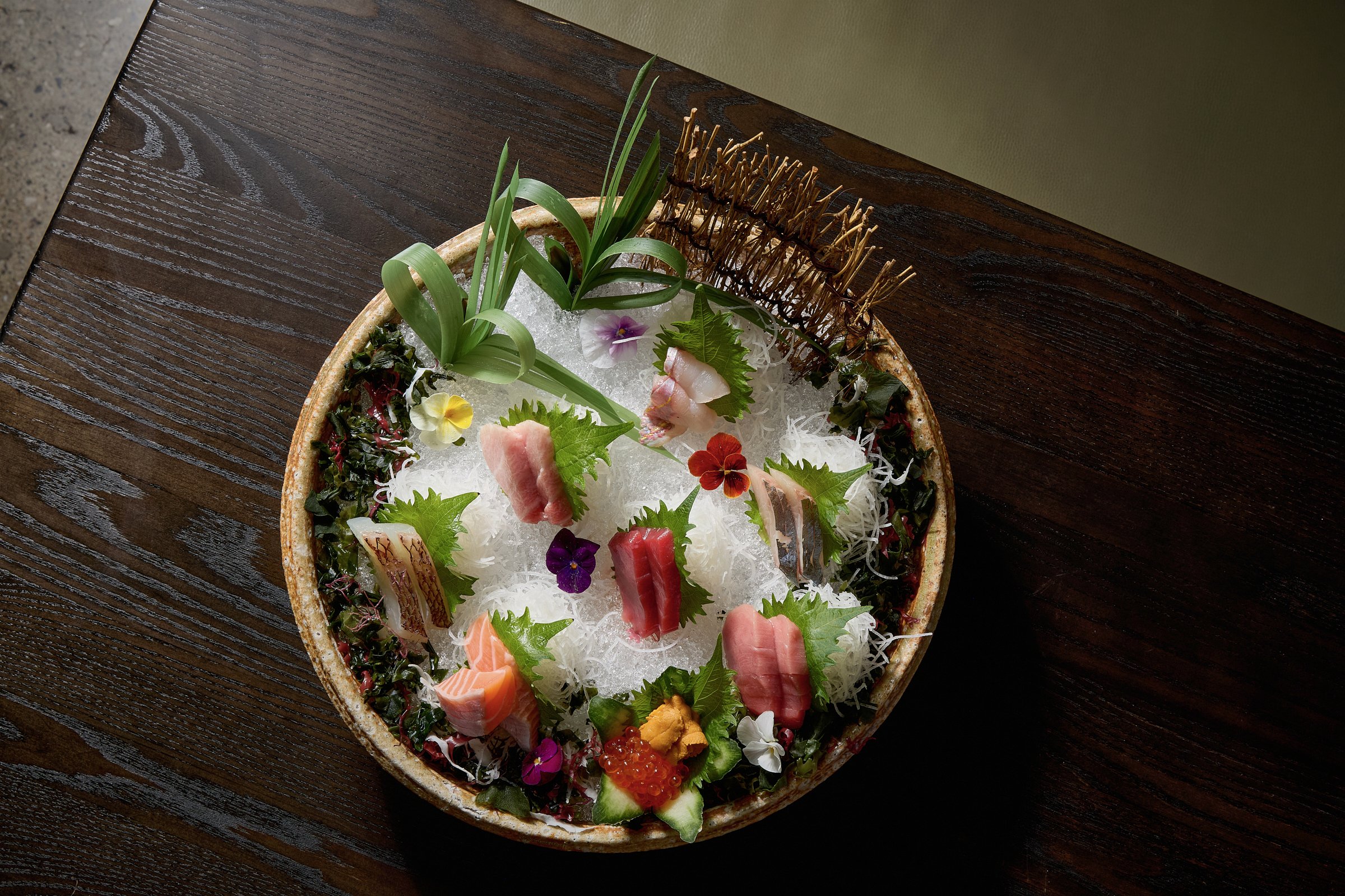 Assorted sashimi arranged on a decorative plate with garnishes and edible flowers, served on a bed of shredded daikon.
