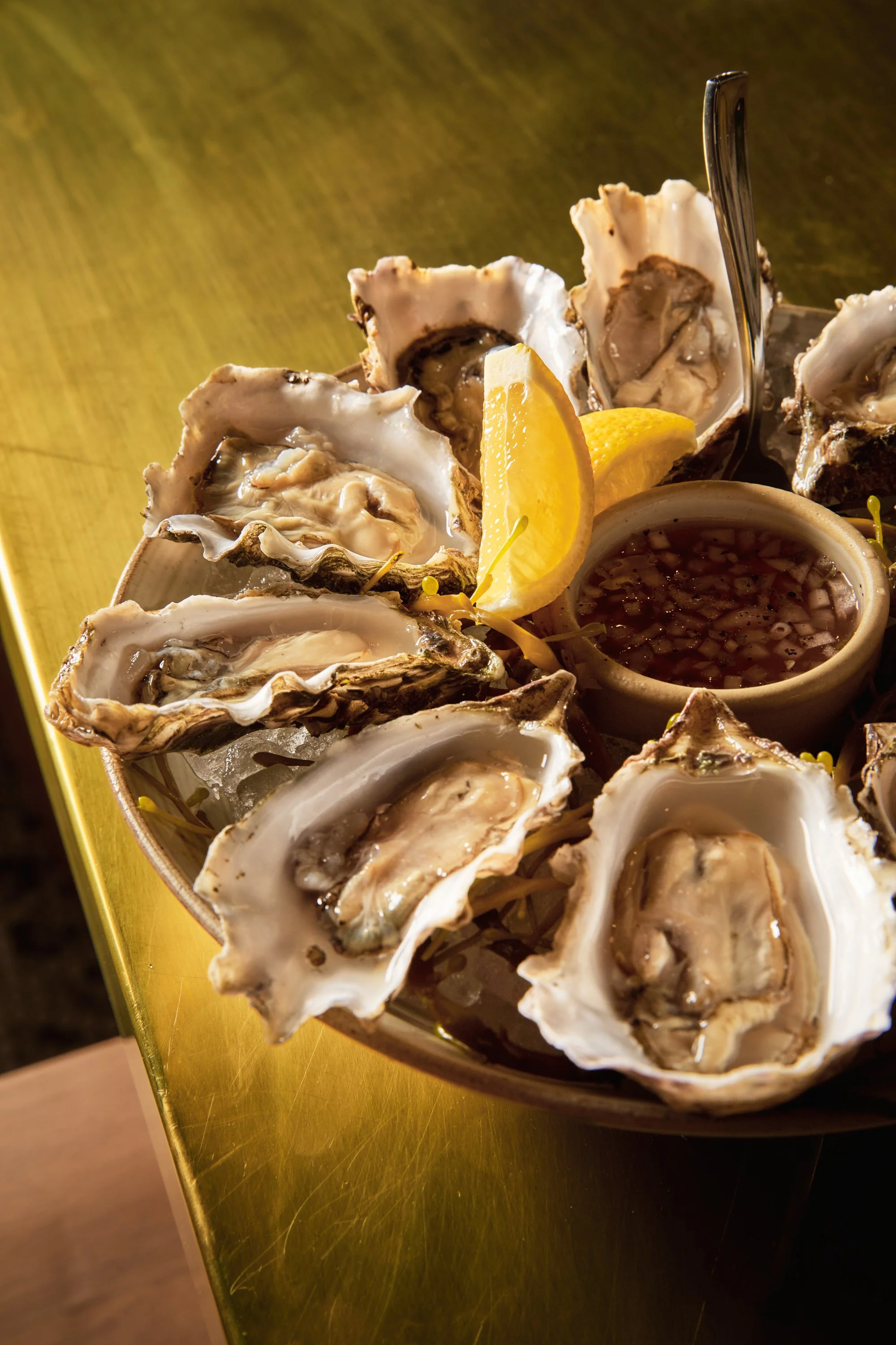Fresh oysters on a bed of ice with lemon wedges and cocktail sauce in a bowl.