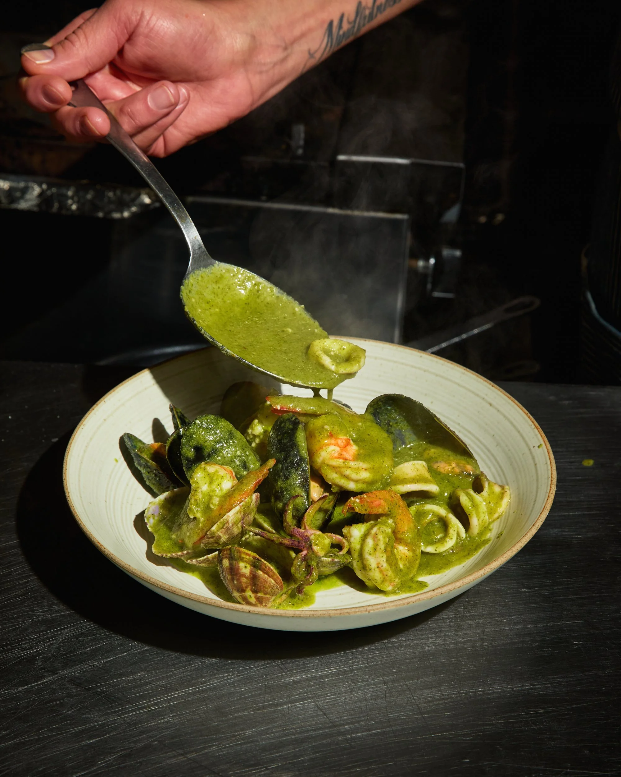 Dish of pasta or seafood with green pesto or herb sauce, served with shellfish and mussels in a white bowl