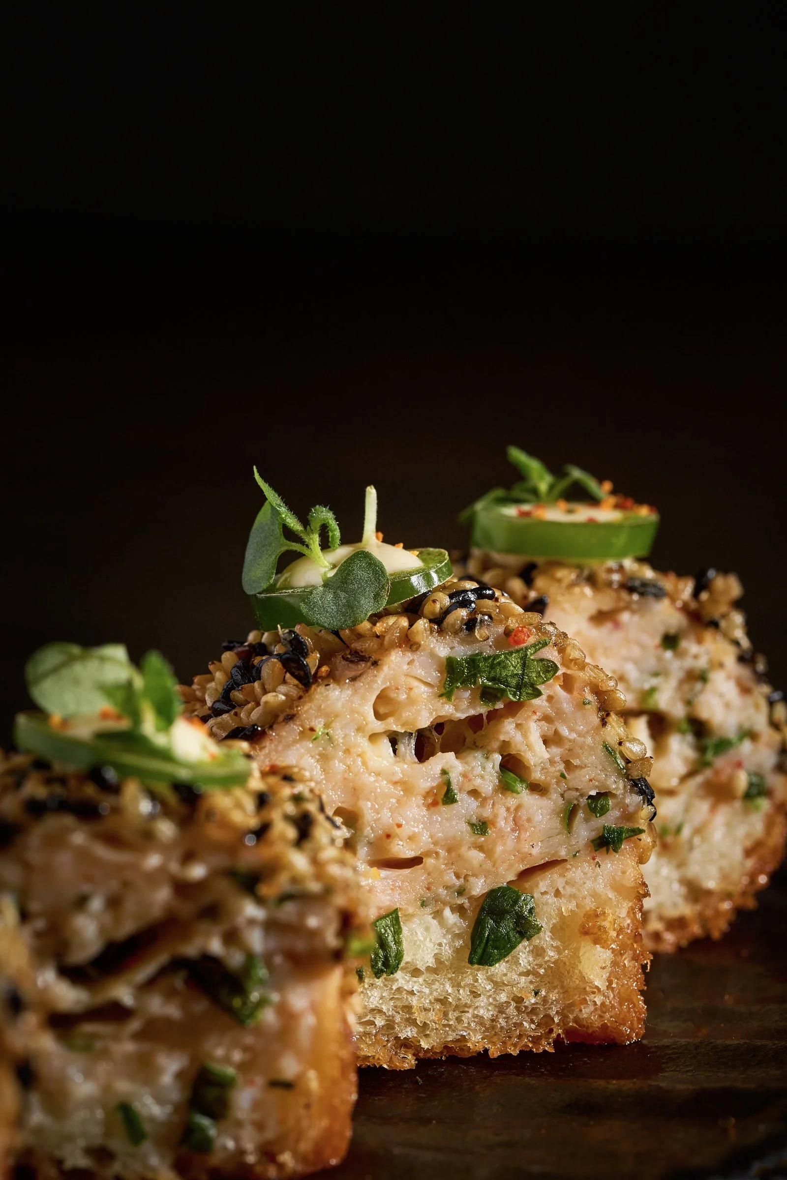 Close-up of three slices of savory bread pudding topped with microgreens against a dark background.
