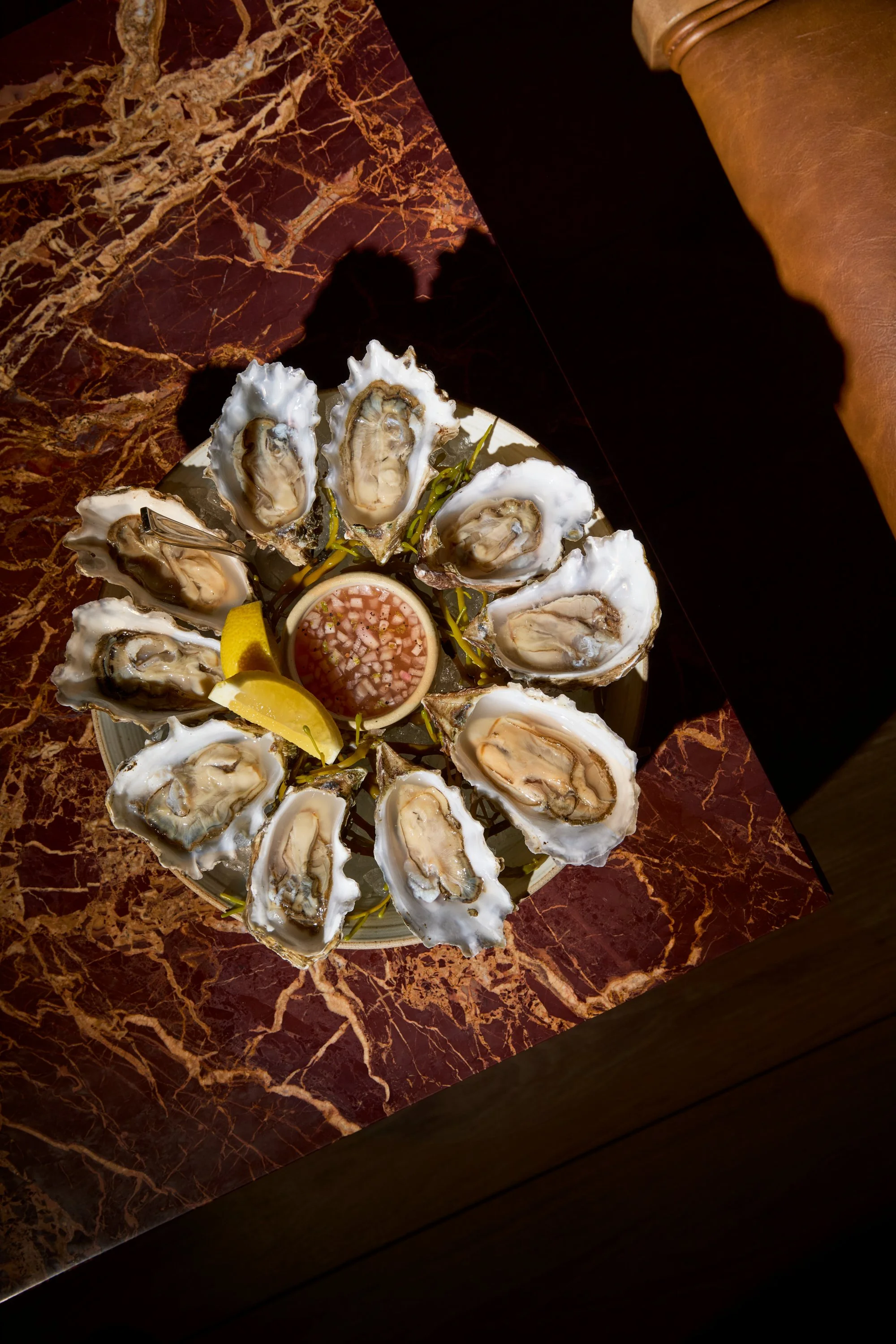 A plate of raw oysters on the half shell with lemon wedges and cocktail sauce on a marble table.