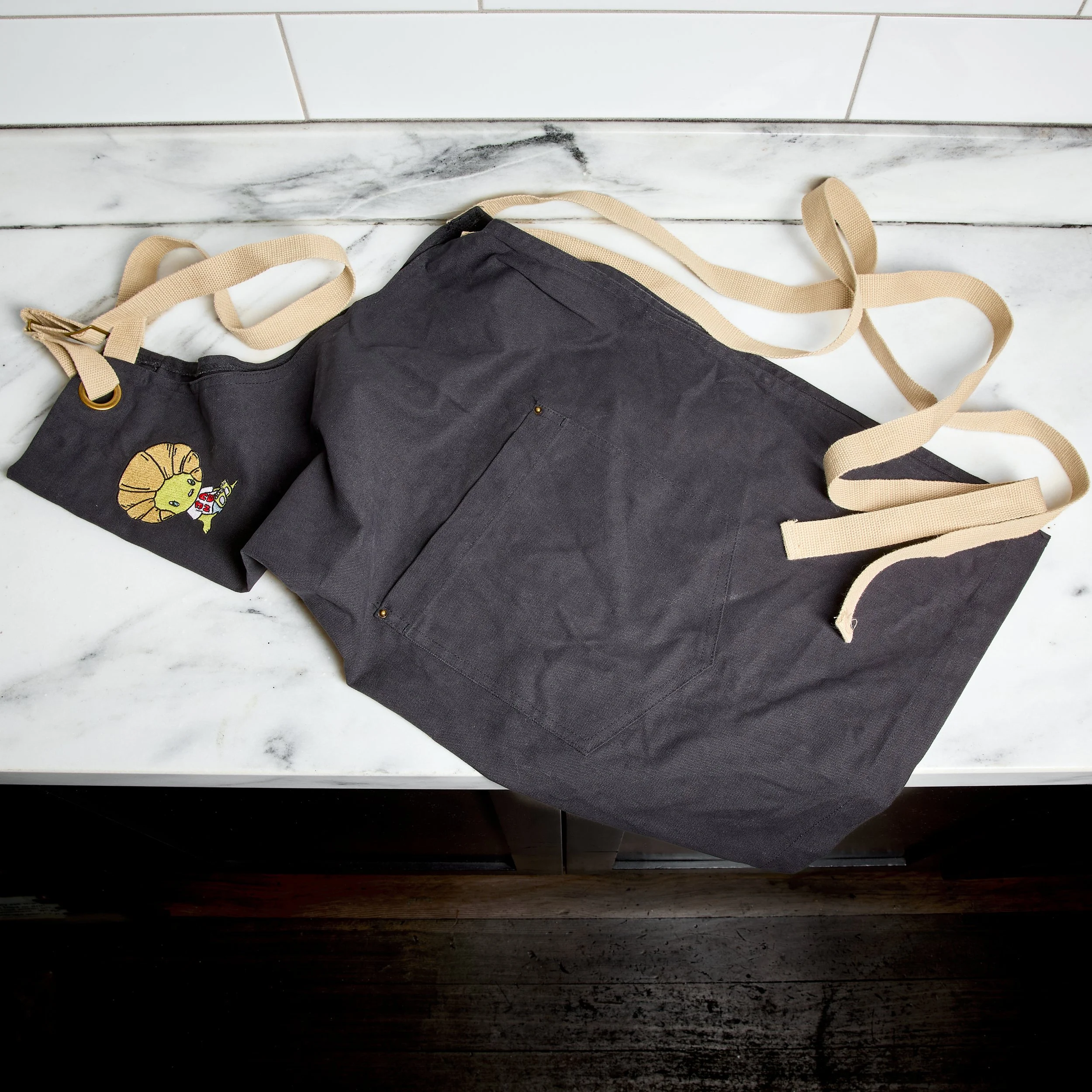 A gray apron with beige straps lying on a white marble countertop.