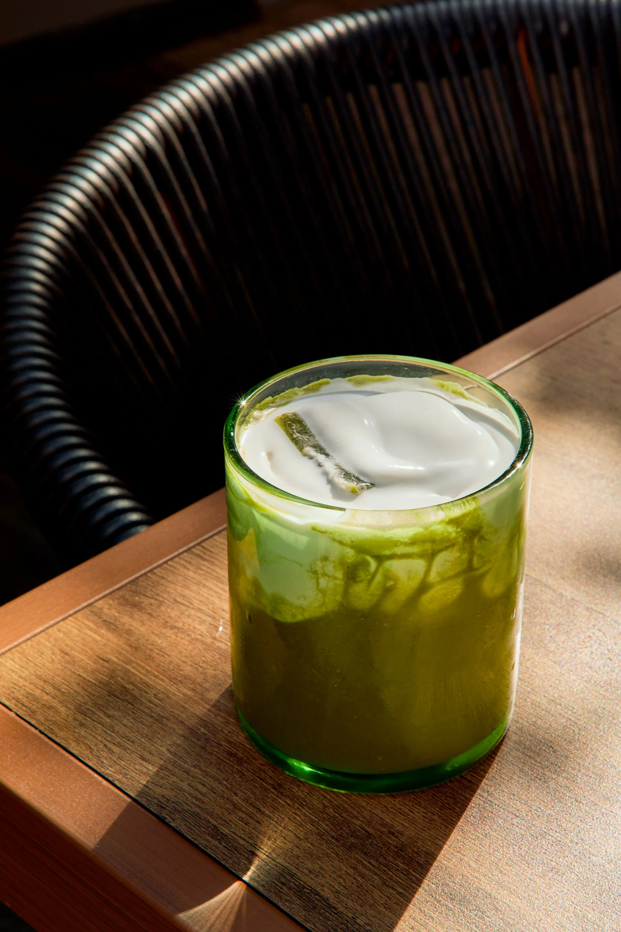 Close-up of a green and white layered drink with a straw, on a wooden table.