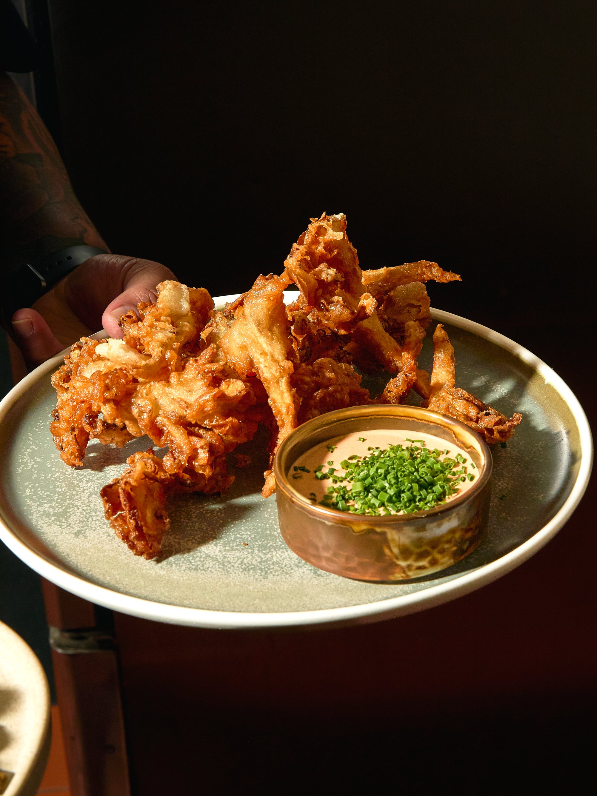 Fried chicken wings on a plate with a side of dipping sauce sprinkled with chopped green onions.