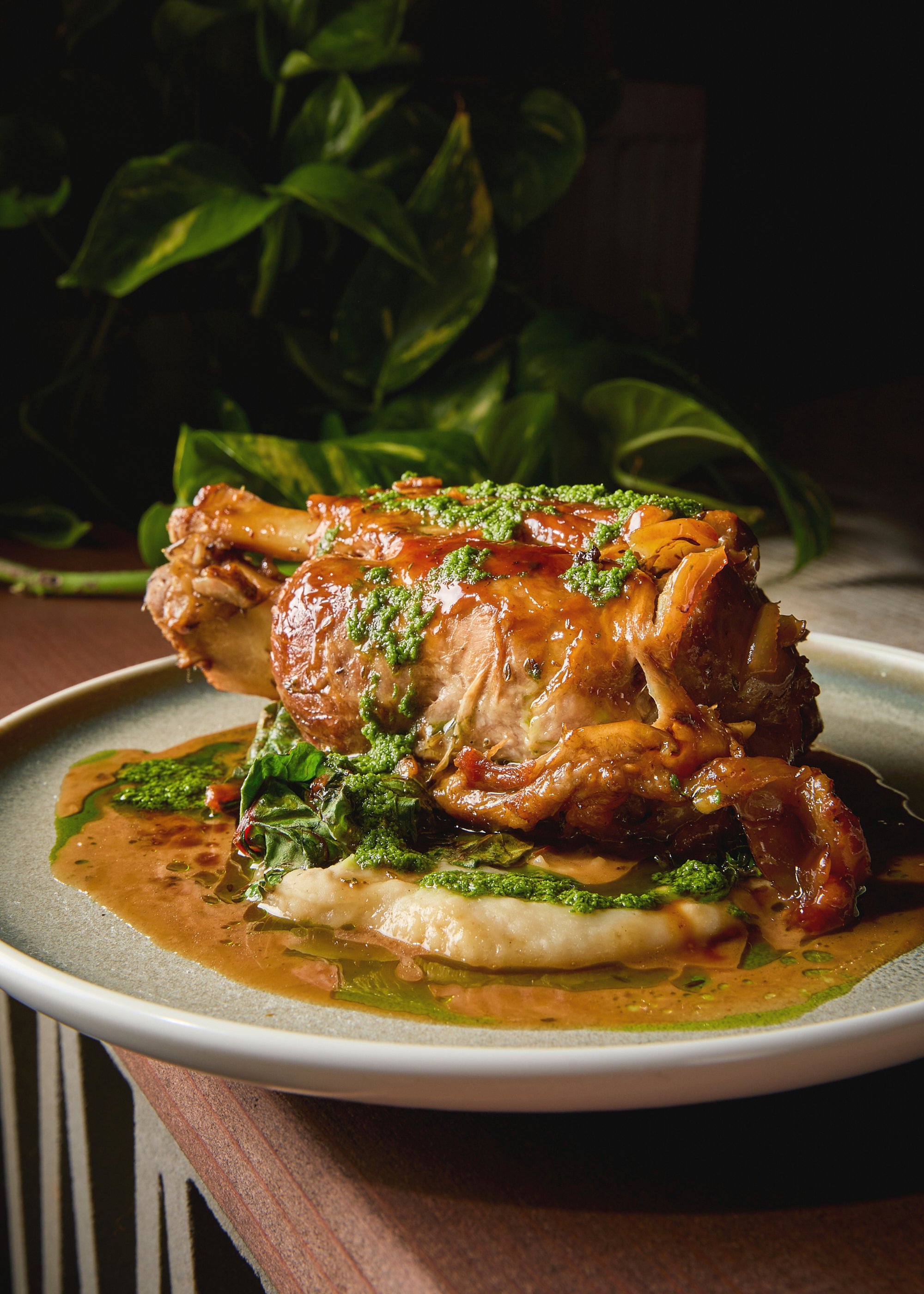 A plated roasted meat dish with sauce and greens on a beige plate.