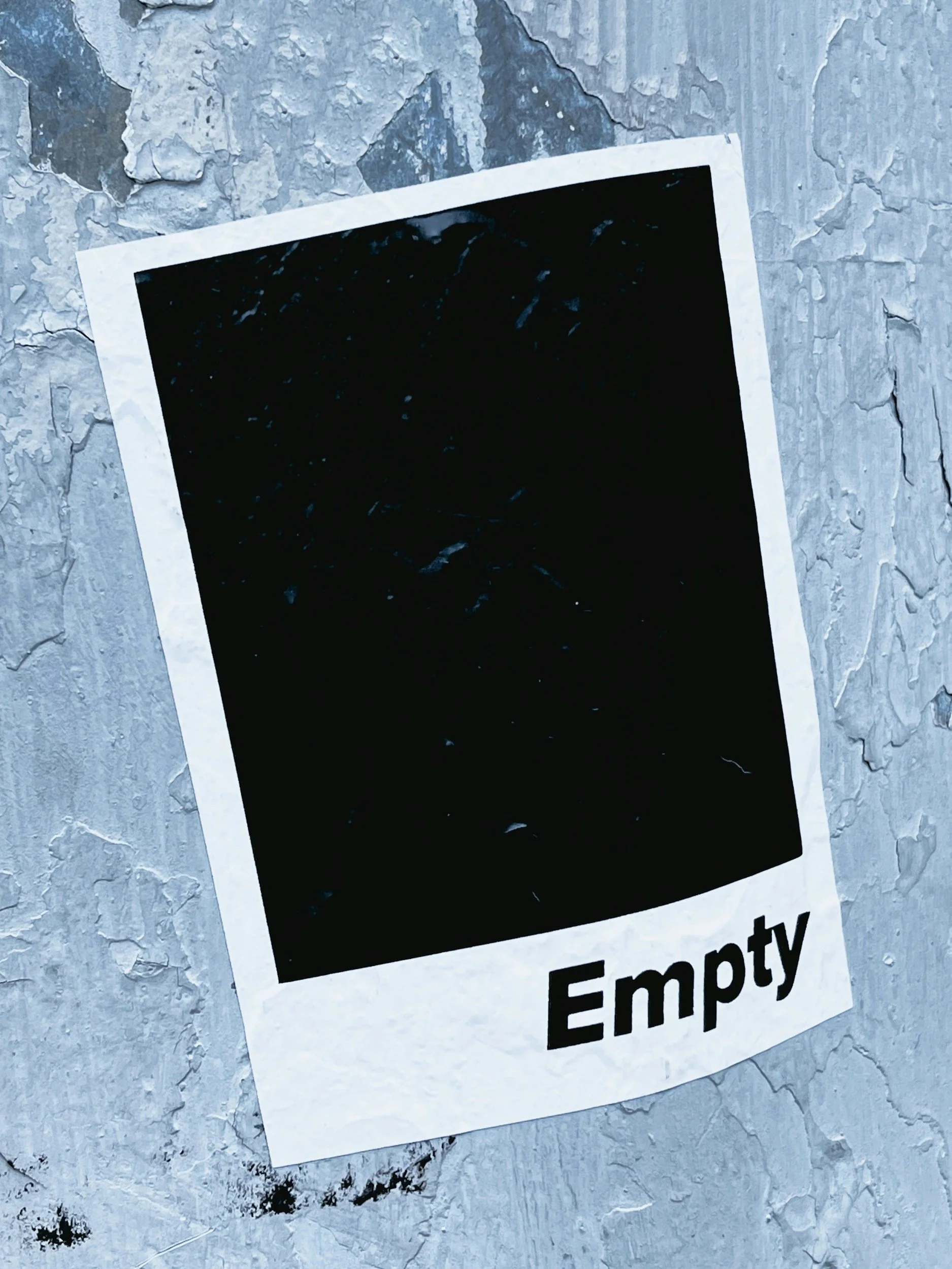 A blank instant photo with the word "Empty" written at the bottom, placed on a textured, weathered gray surface.