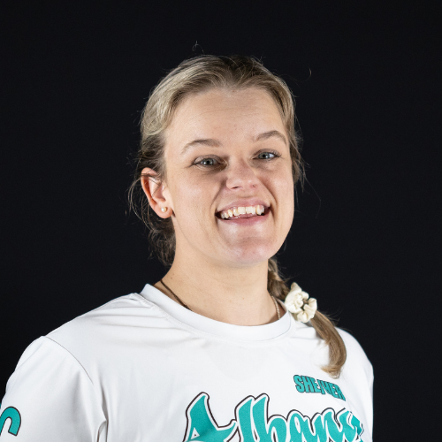 A young woman with blonde hair in a braid, smiling, wearing a white sports jersey with blue and black text on a black background.