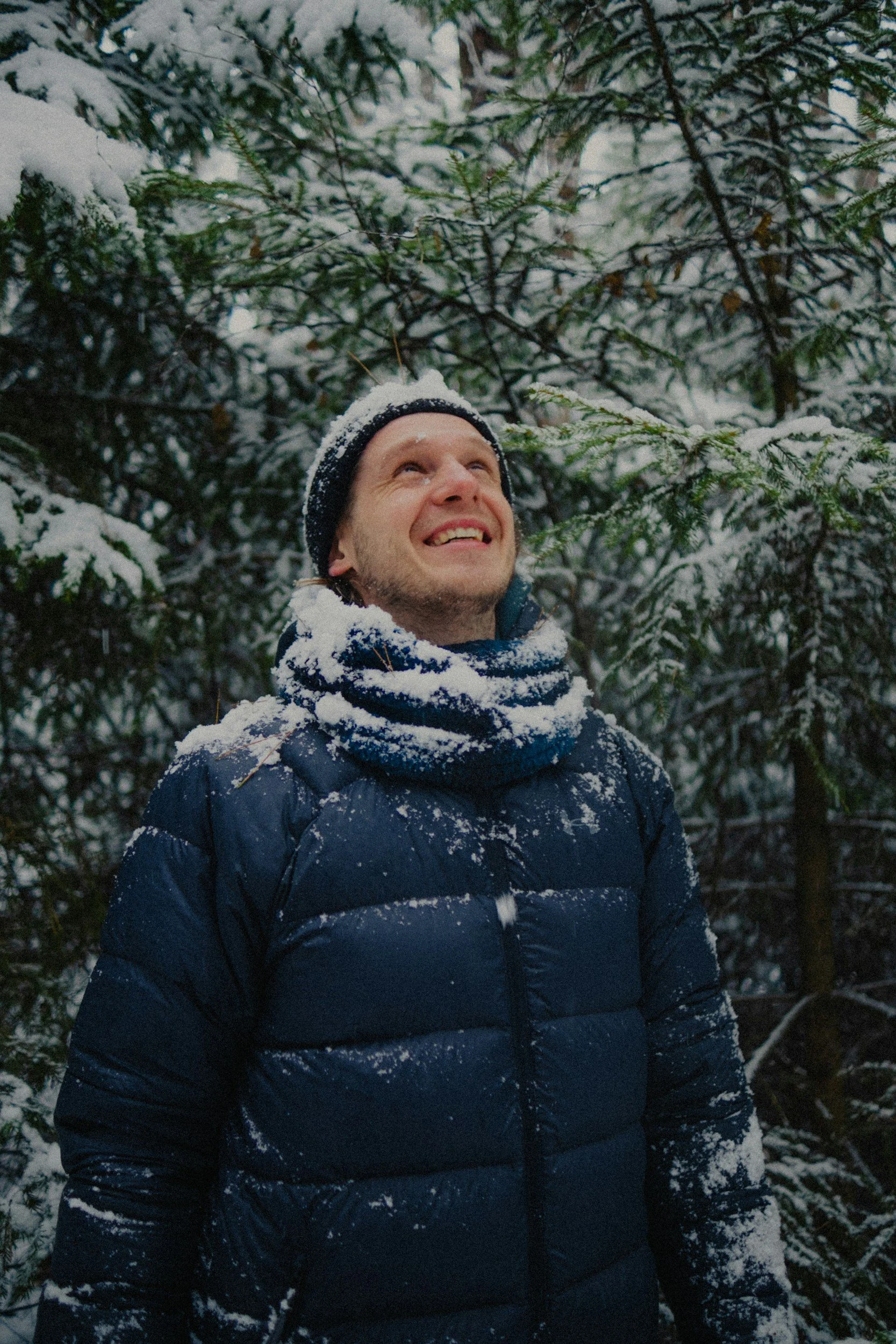Man in winter coat dusted in snow when woods in the background