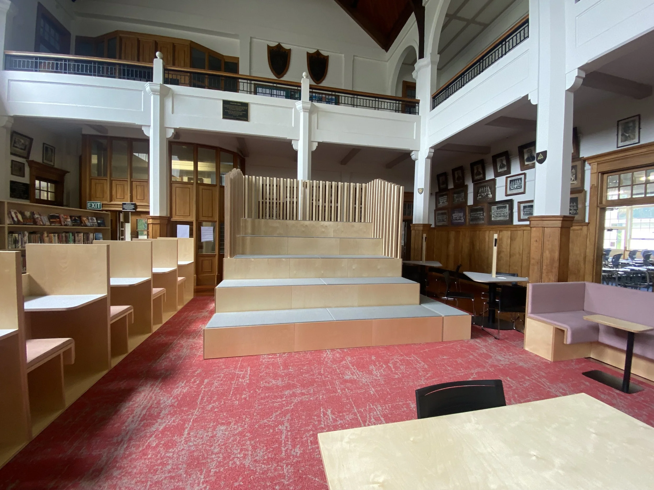 Interior of a library with wooden paneling, bookshelves, and a stage in the center.