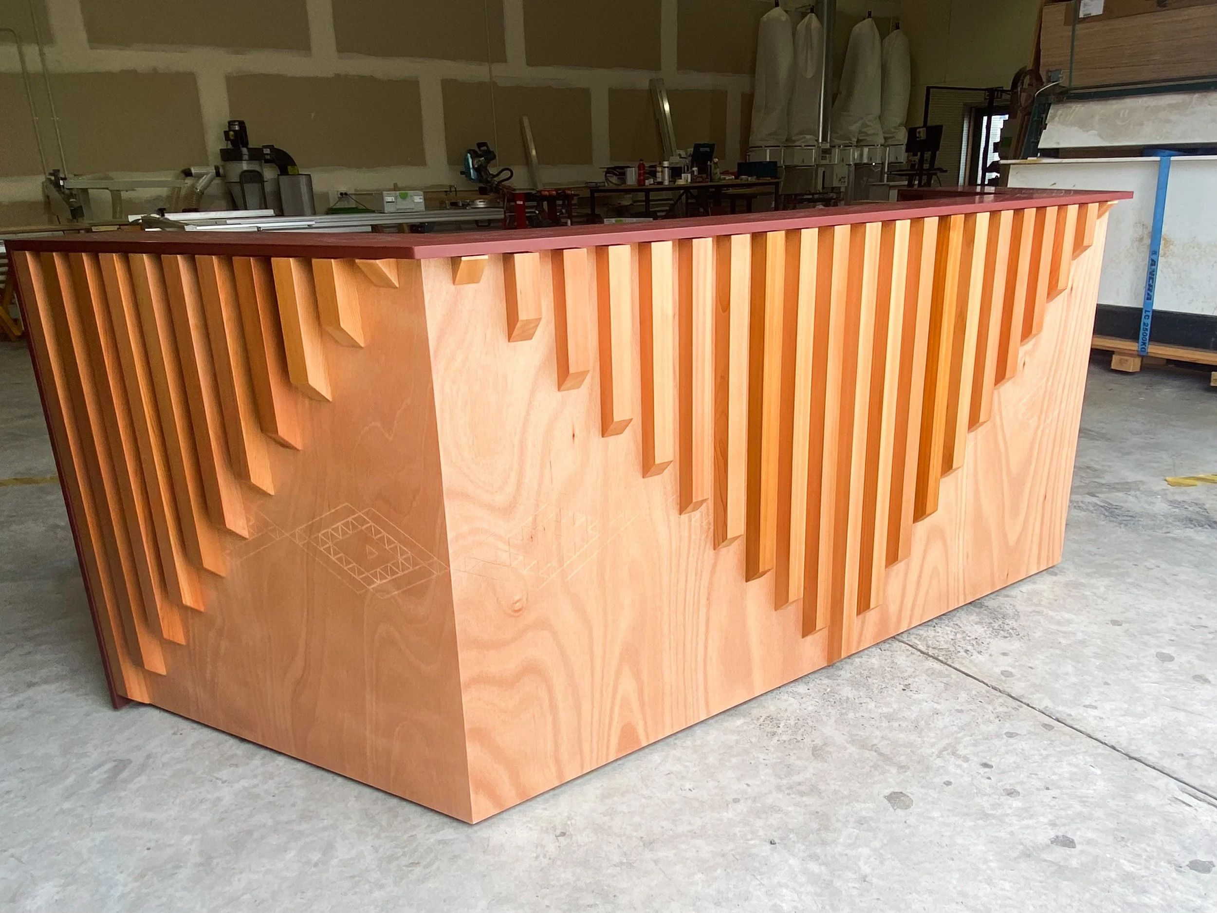 A wooden reception desk with a decorative slat design on the front in a workshop setting.