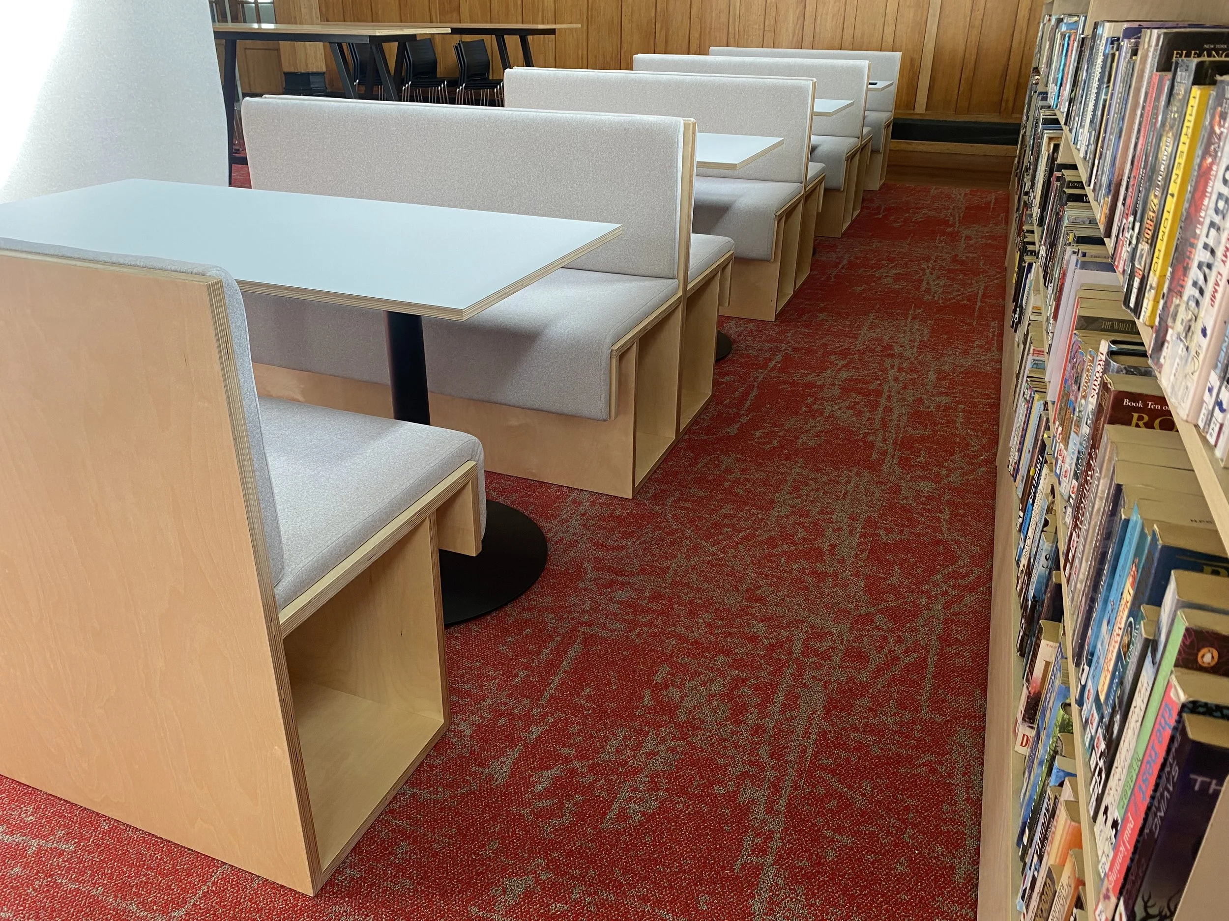 Bookshelves filled with books on the right, with tables and chairs on the left in a library reading area.