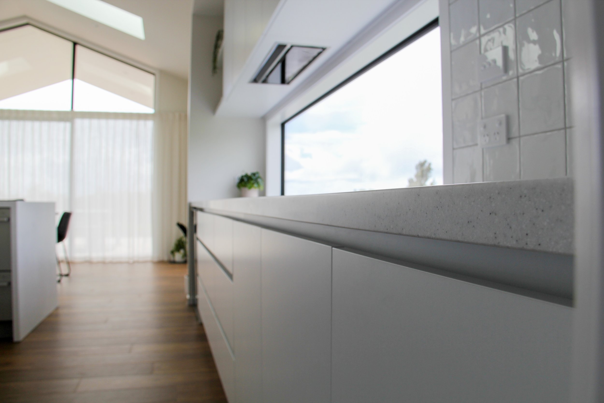 Modern kitchen with white cabinets, a large window, and a potted plant, with a view of brown hardwood floors and natural light.