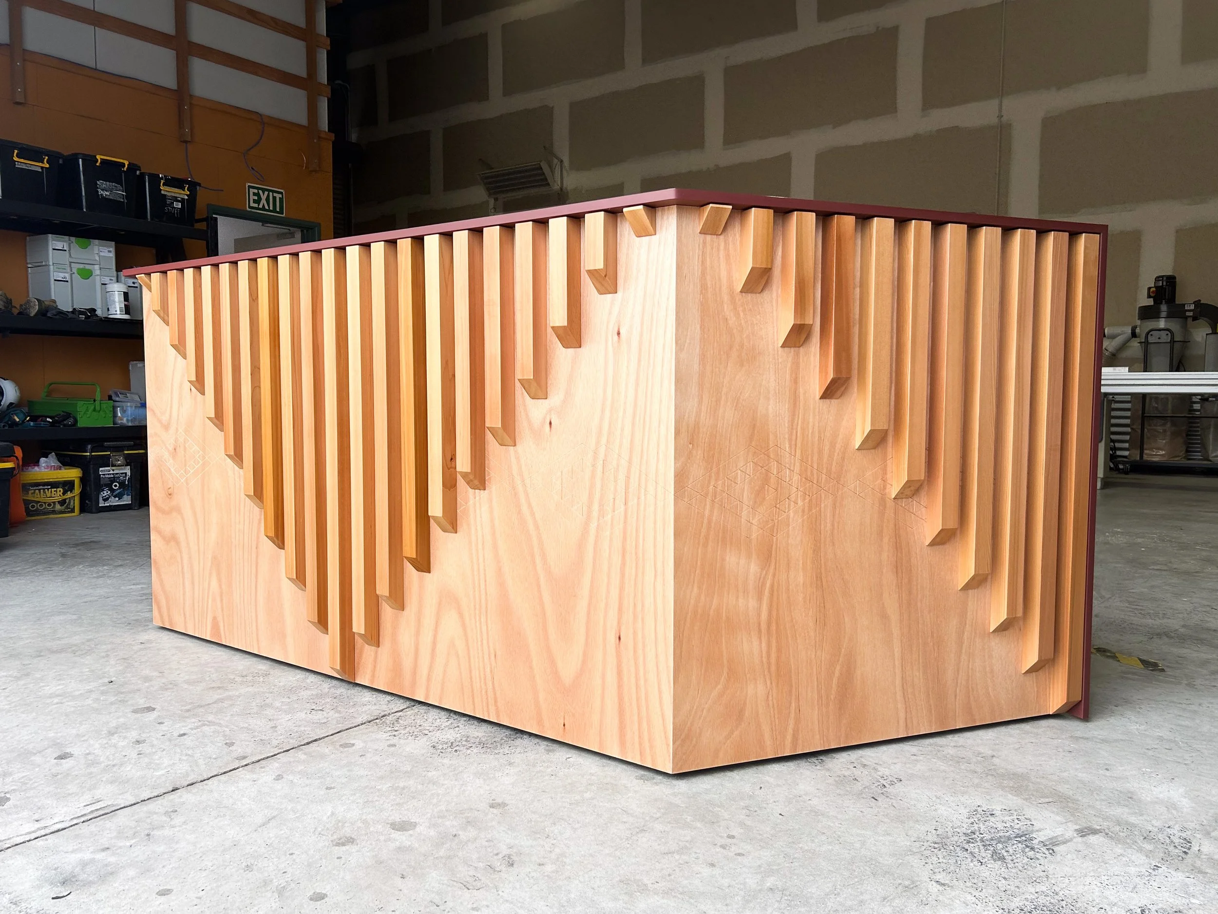 A wooden piece of furniture with vertical wooden slats arranged in a pattern, in a workshop setting.