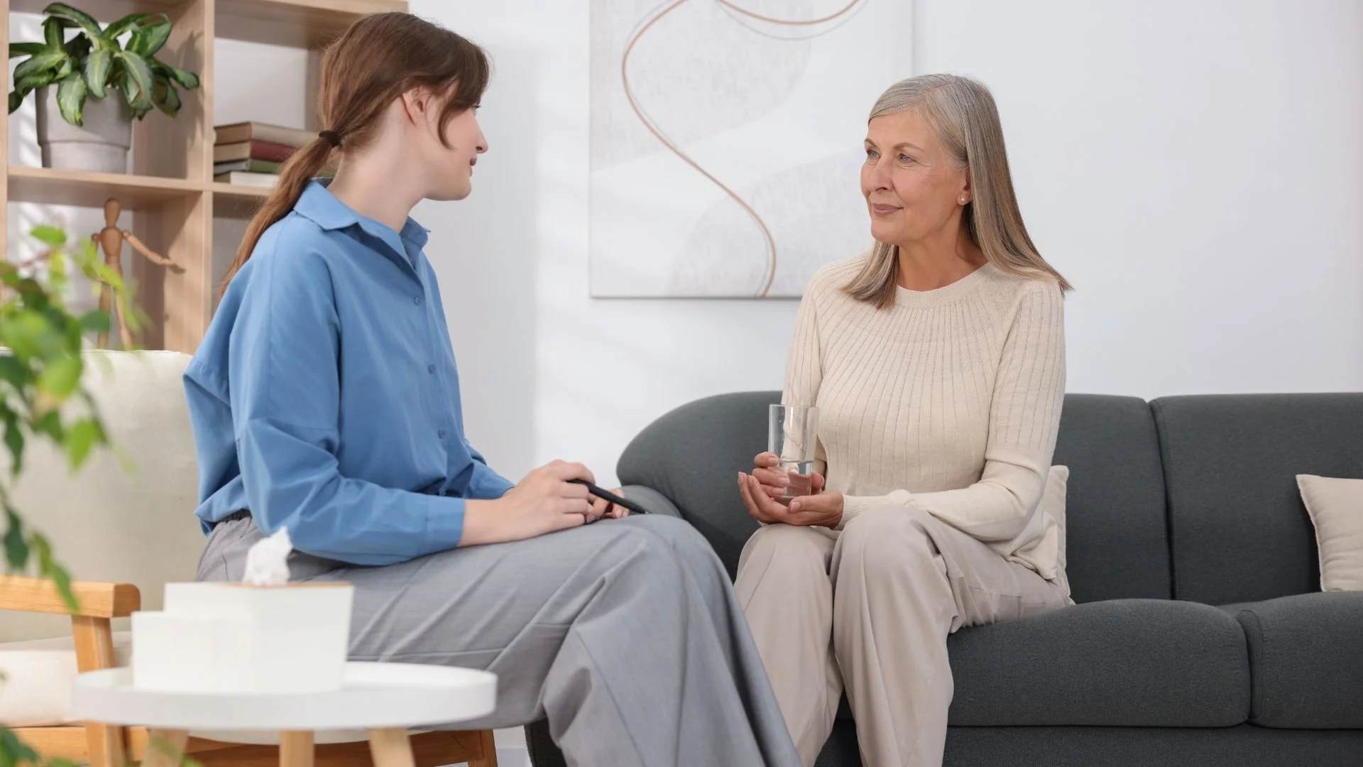 A professional psychotherapist listening to a patient during a mental health therapy session in a modern office setting.