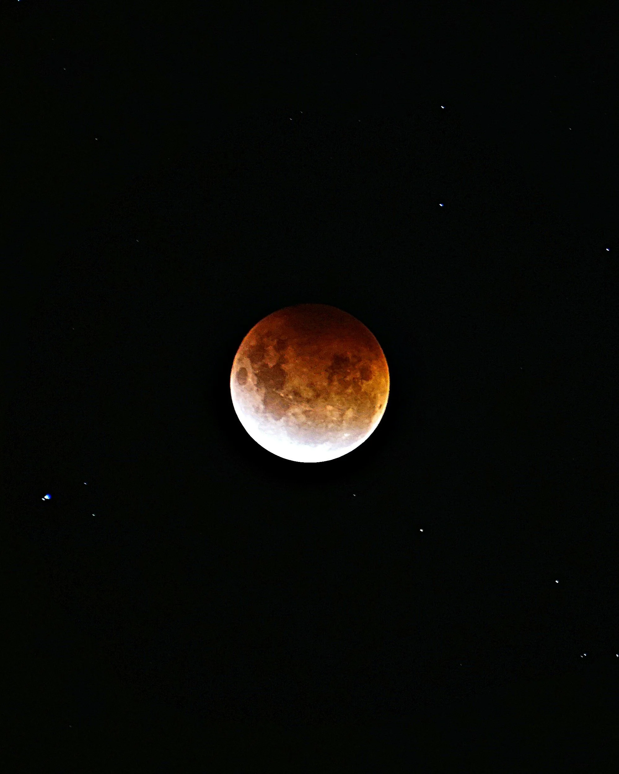 Lunar eclipse showing the moon with a reddish hue against a dark night sky with visible stars.