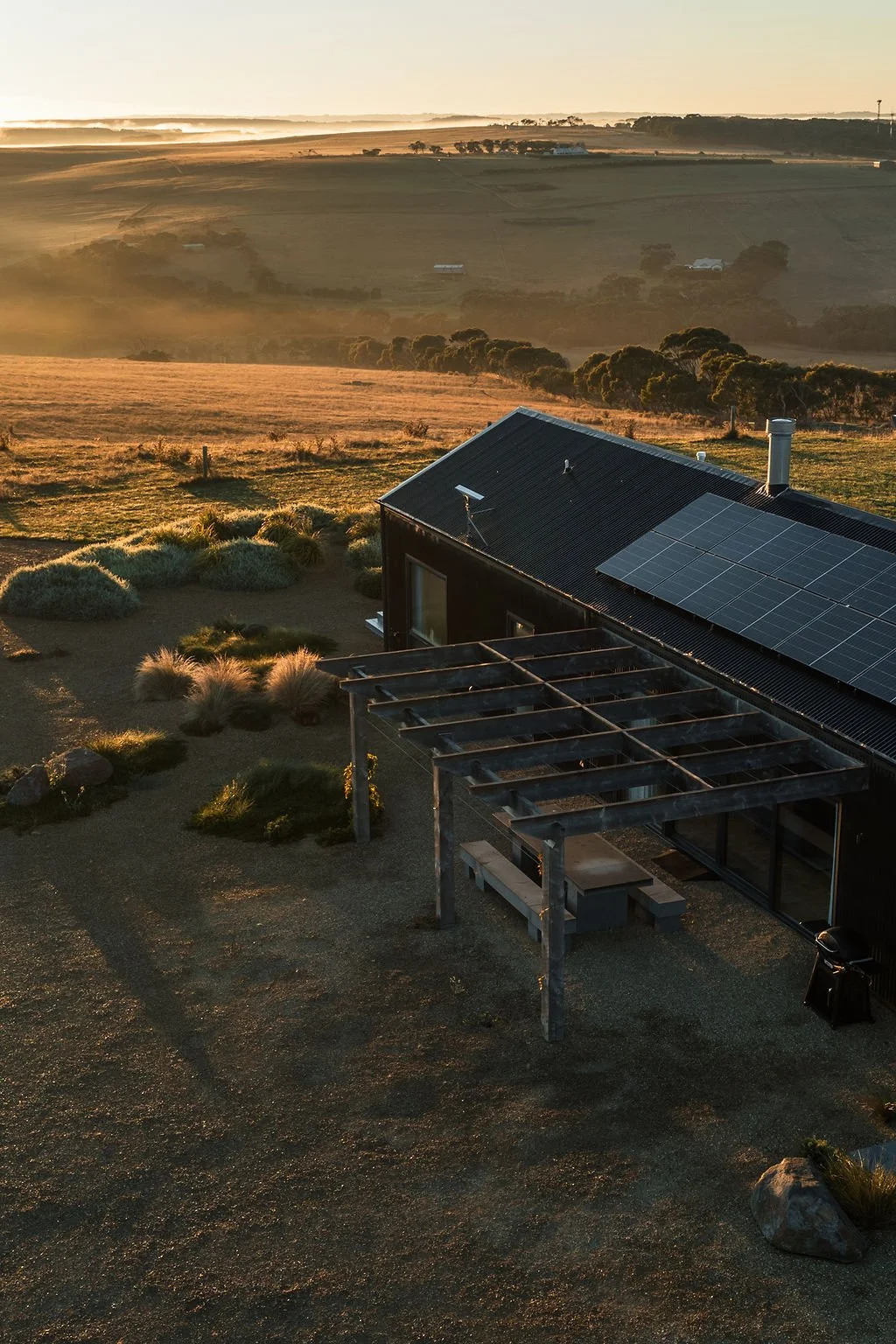 Aerial image of Port Farm at sunrise. A black shed house that is offgrid with soft morning light overlooking the Great Ocean Road Hinterland.
