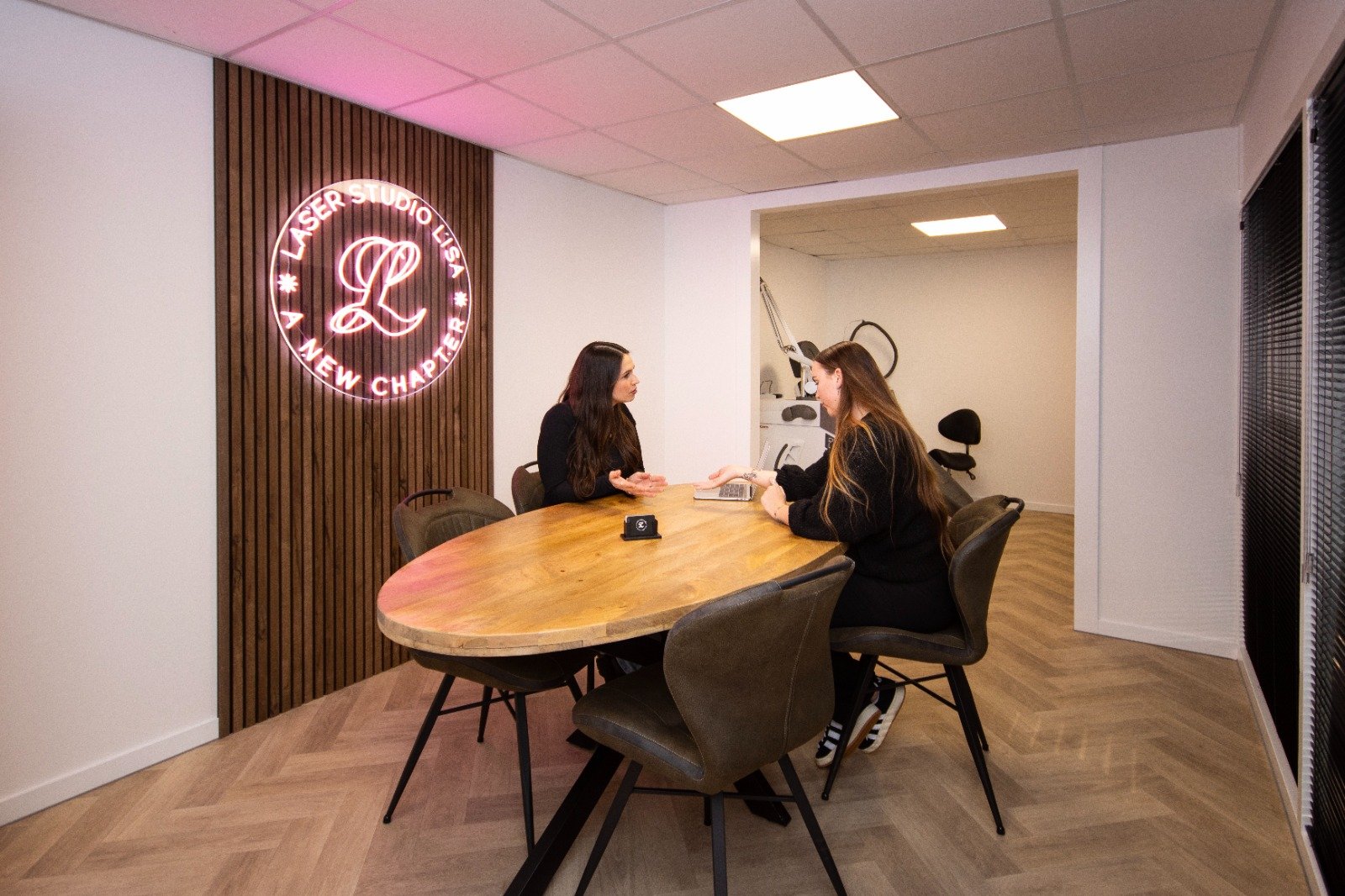 Specialist Lisa tijdens een intakegesprek met een klant in Laser Studio Lisa met het neon studio logo op de achtergrond