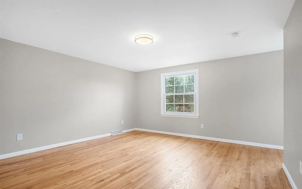 Empty room with light hardwood floors, white window, and freshly painted light tan walls