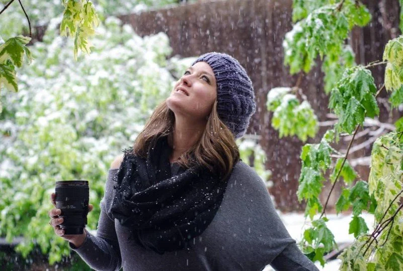 woman wearing a scarf and hat looking up at trees