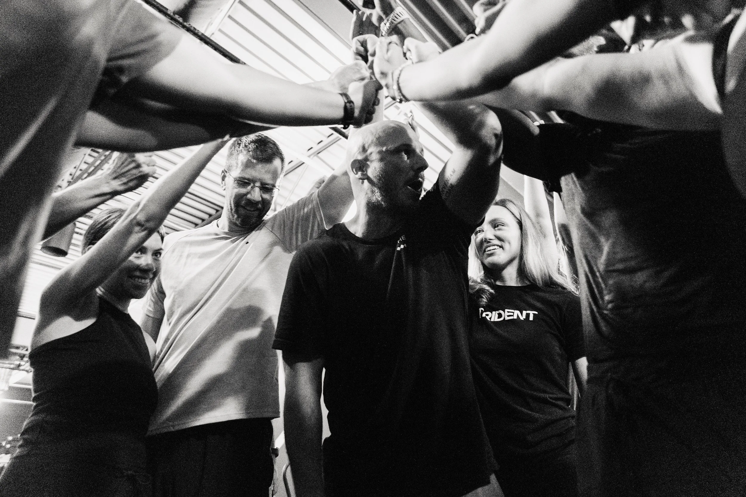 A group of diverse people in athletic clothing forming a circle, holding hands, and showing support during a sports event indoors.
