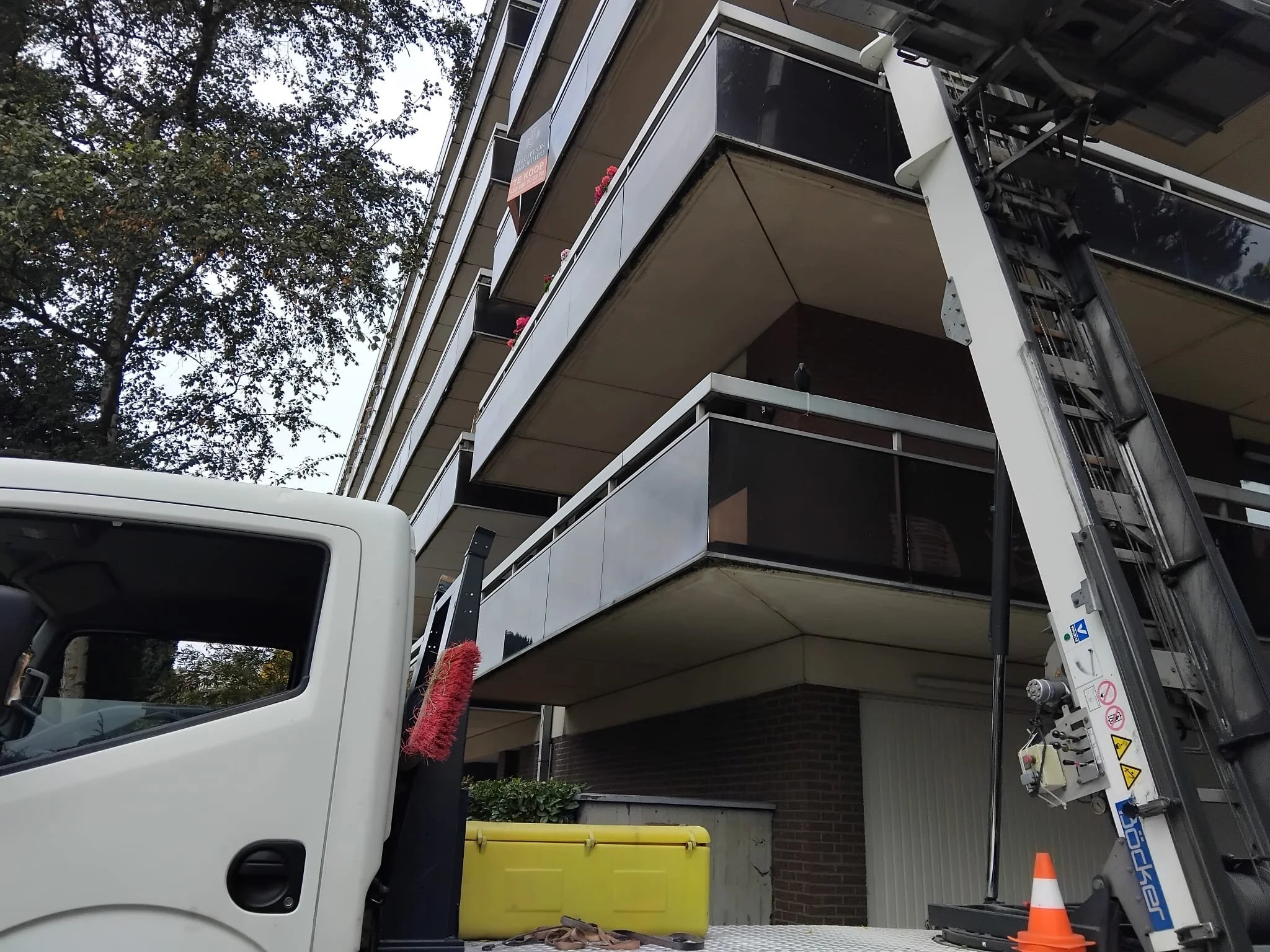 Camion avec une échelle de levage à proximité d'un immeuble résidentiel à plusieurs étages, avec des balcons et des murs en briques rouges.