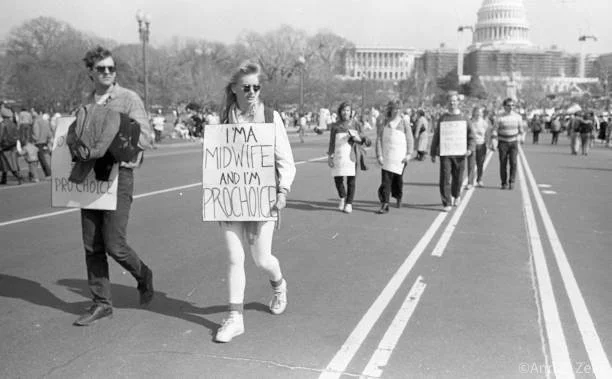 March 09, 1986
View of a Pro Choice demonstrator with a sign that reads 'I'm a Midwife and I'm Pro Choice' on Pennsylvania Avenue NW (near 3rd St SW) during the March for Women's Lives, Washington DC, March 9, 1986. Visible in the background is the U